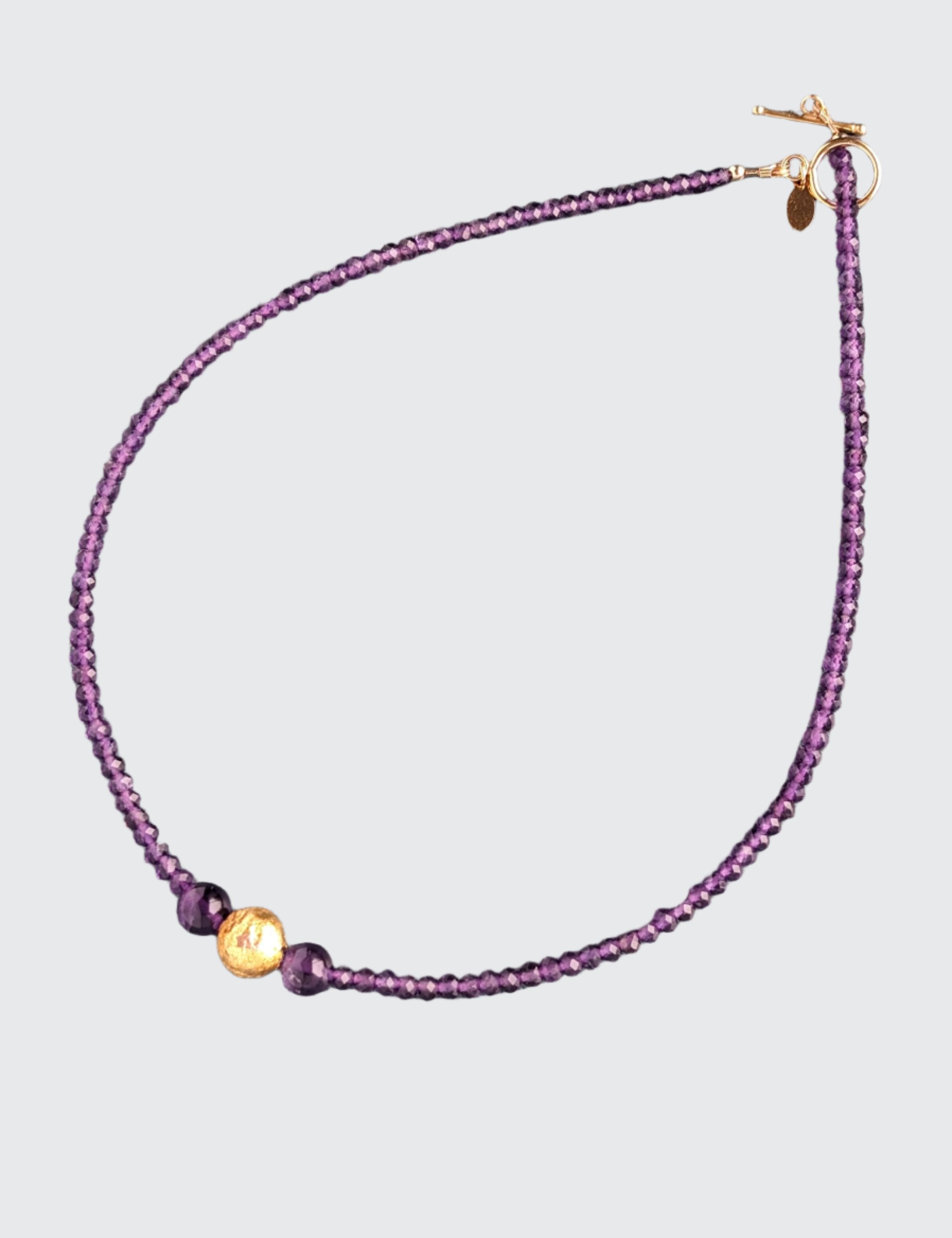 Amethyst Glow Necklace. Handcrafted with exquisite attention to detail, this elegant piece features stunning amethyst gemstones complemented by hand-gilded 23 karat gold leaf on lava stone center bead. It measures 17-inch in length and is finished with a 14 karat gold-filled toggle clasp.