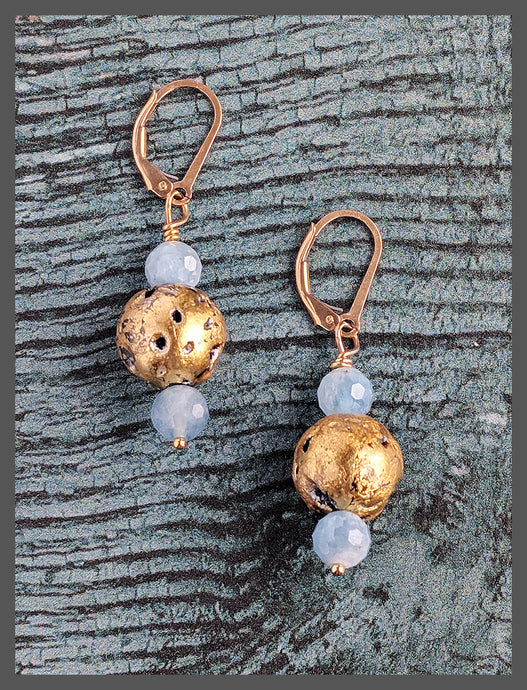 The Aquamarine Glow earrings are lightweight drop earrings featuring light blue aquamarine beads and 23-karat gold leaf on lava stones. They have a dainty, heirloom-like quality with a natural and elegant texture. The faceted aquamarine beads and 14-karat gold-filled leverback findings add delicate charm. The earrings measure 1.5