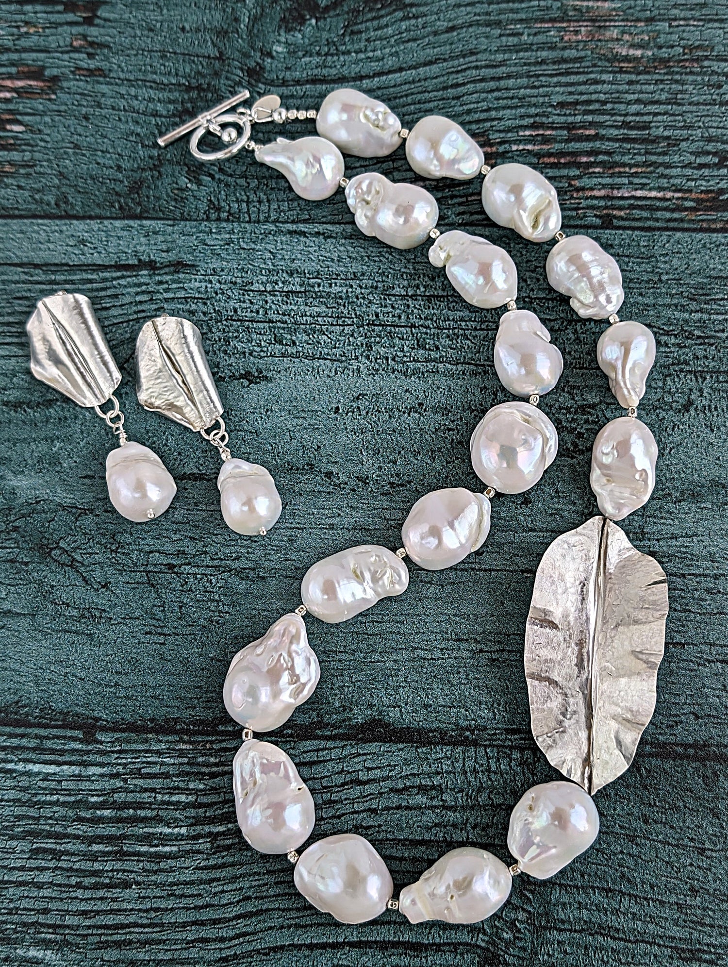 Shown together are White Baroque pearl and silver necklace and earrings with hammered and fold form leaf design in silver with small silver beads in between each pearl. Necklace is finished with silver toggle clasp and designer tag.