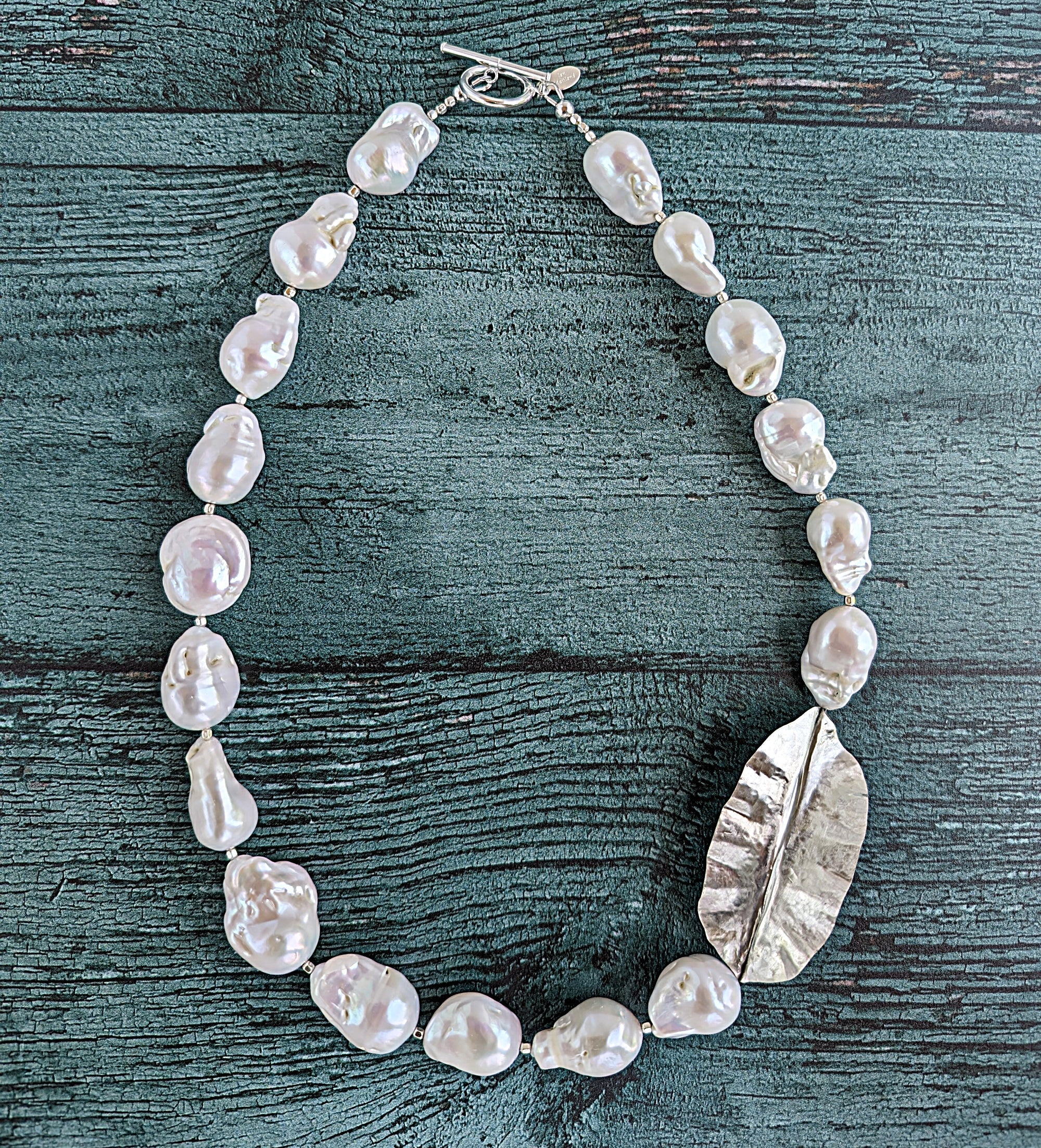 White Baroque pearl and silver necklace with hammered and fold form leaf design in silver with small silver beads in between each pearl. Necklace is finished with silver toggle clasp and designer tag.