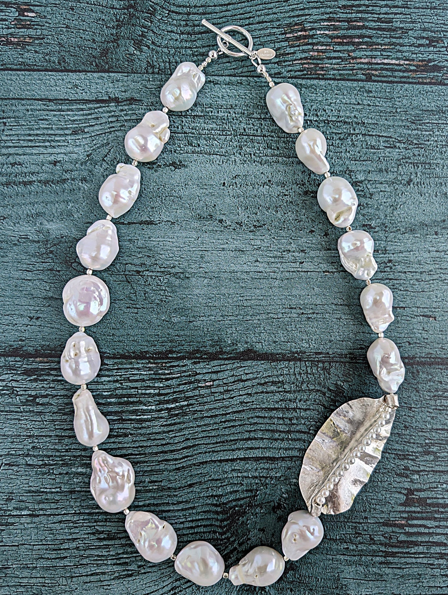 White Baroque pearl and silver necklace with hammered and fold form leaf design in silver with small silver beads in between each pearl. Necklace is finished with silver toggle clasp and designer tag.