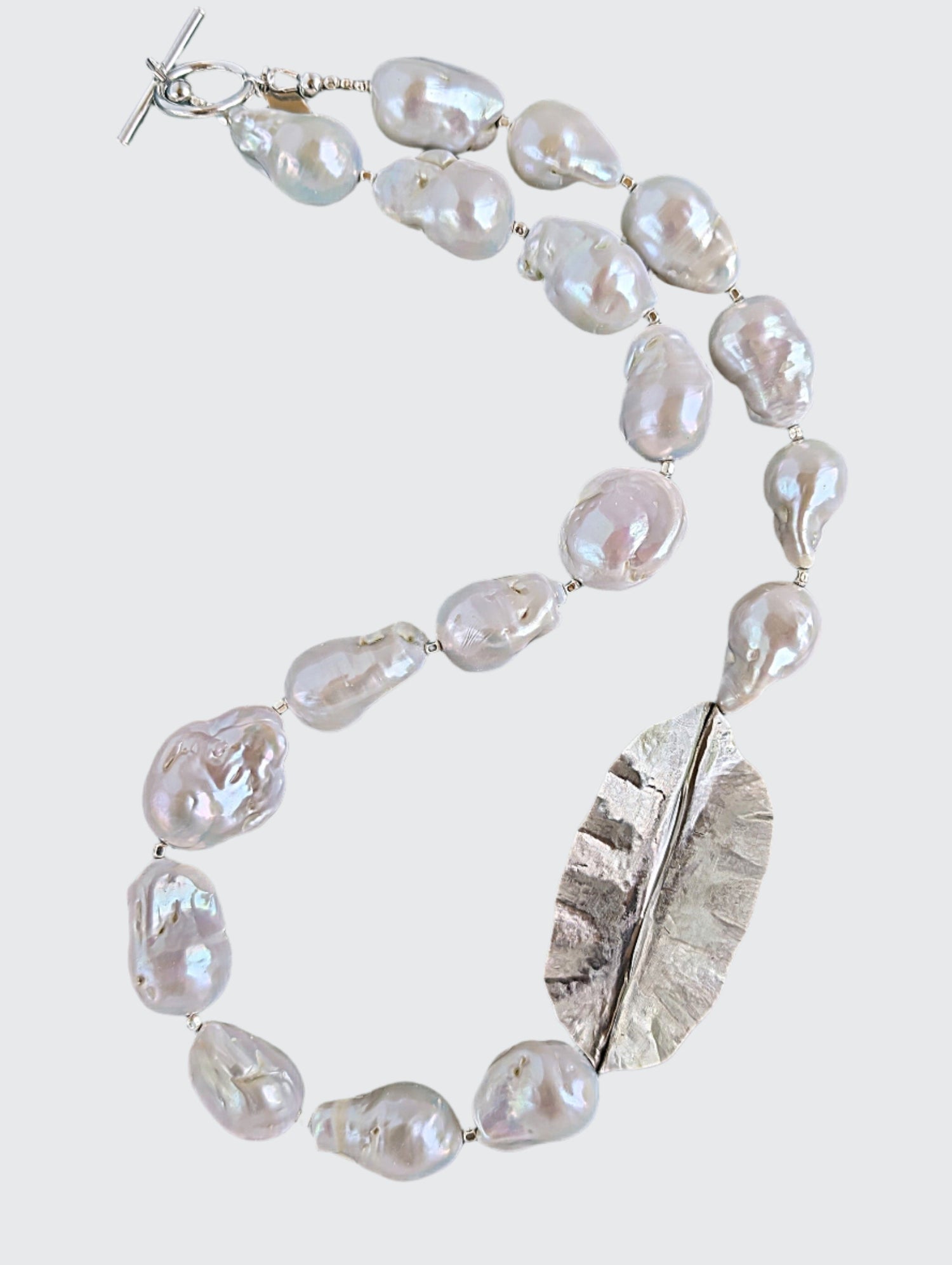 White Baroque pearl and silver necklace with hammered and fold form leaf design in silver with small silver beads in between each pearl. Necklace is finished with silver toggle clasp and designer tag.