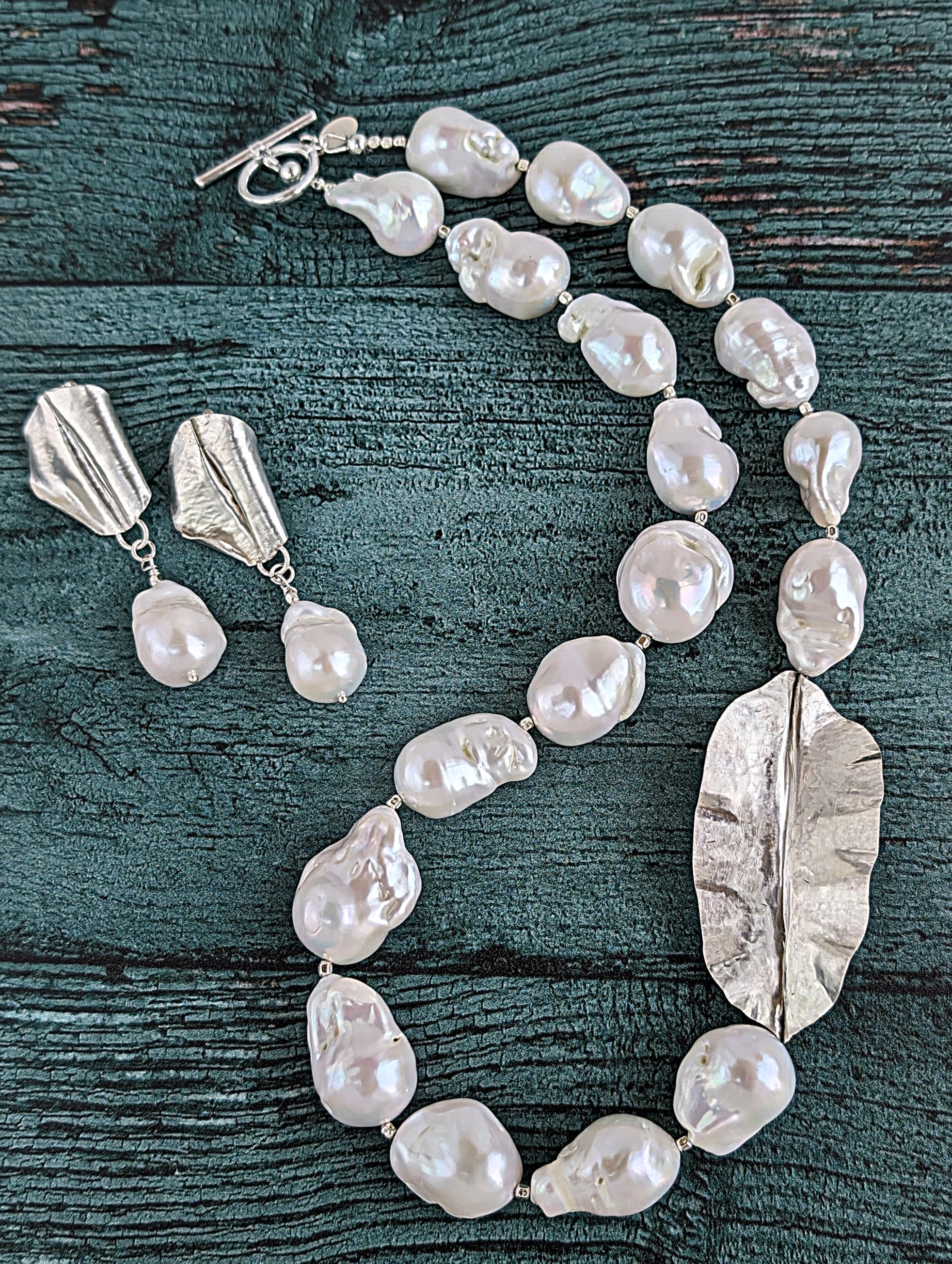 Shown together are White Baroque pearl and silver necklace and earrings with hammered and fold form leaf design in silver with small silver beads in between each pearl. Necklace is finished with silver toggle clasp and designer tag.