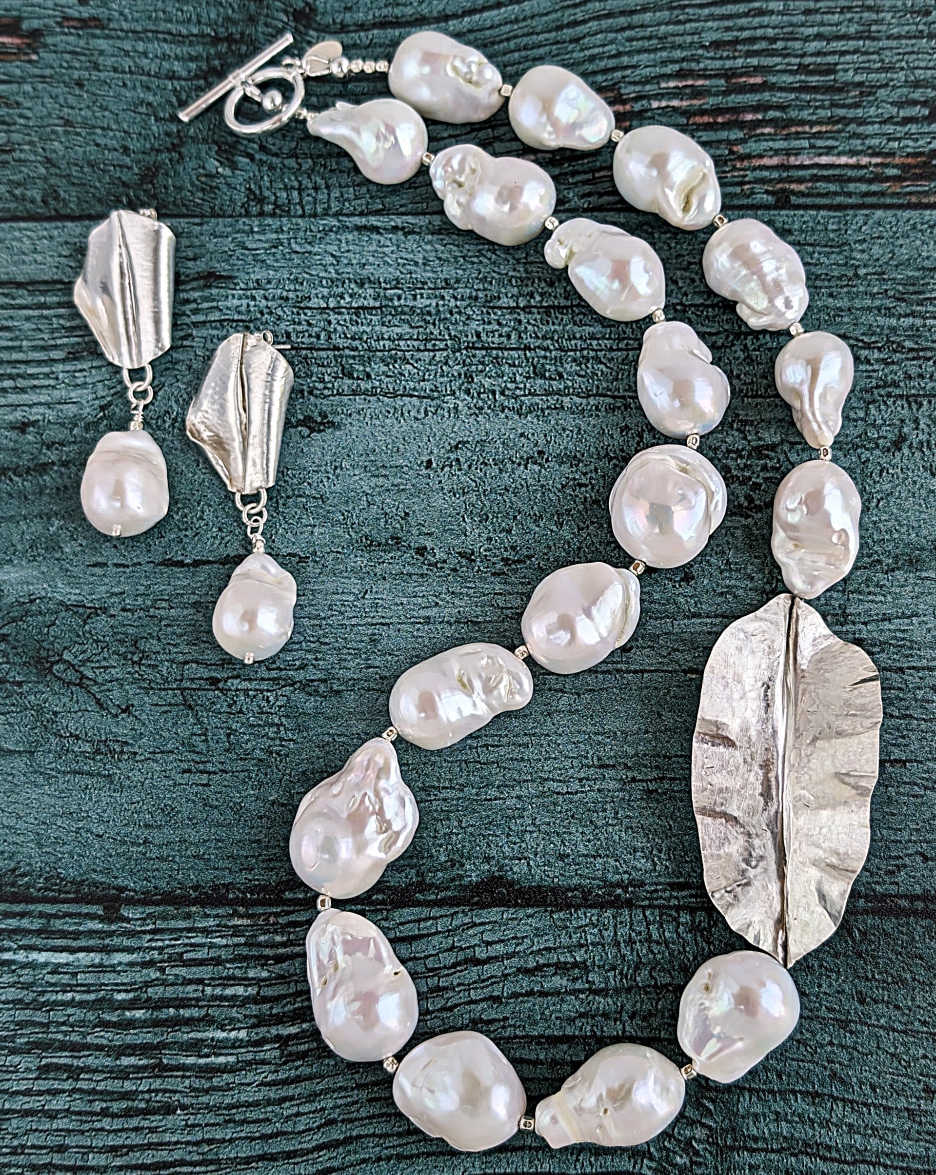 Shown together are White Baroque pearl and silver necklace and earrings with hammered and fold form leaf design in silver with small silver beads in between each pearl. Necklace is finished with silver toggle clasp and designer tag.