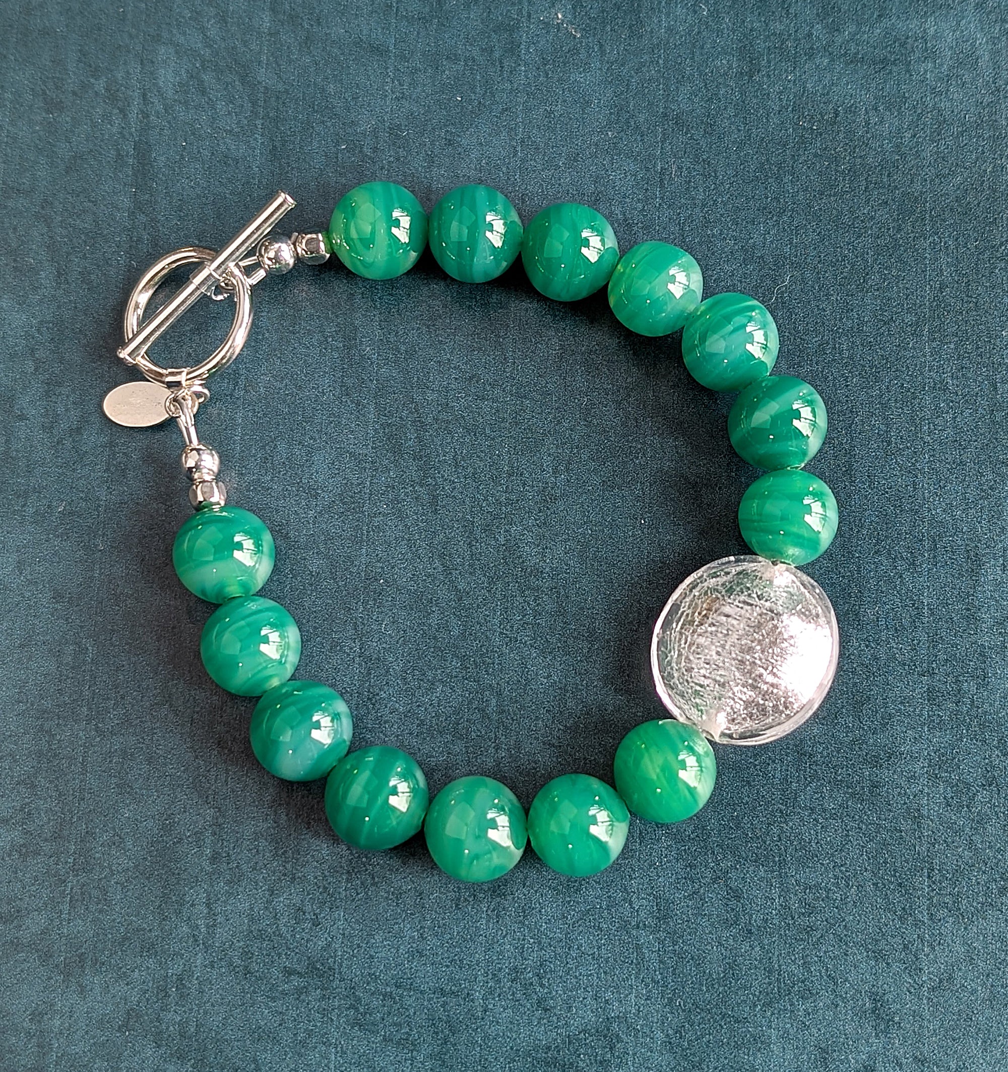 Green beaded bracelet with a silver clasp on a teal background