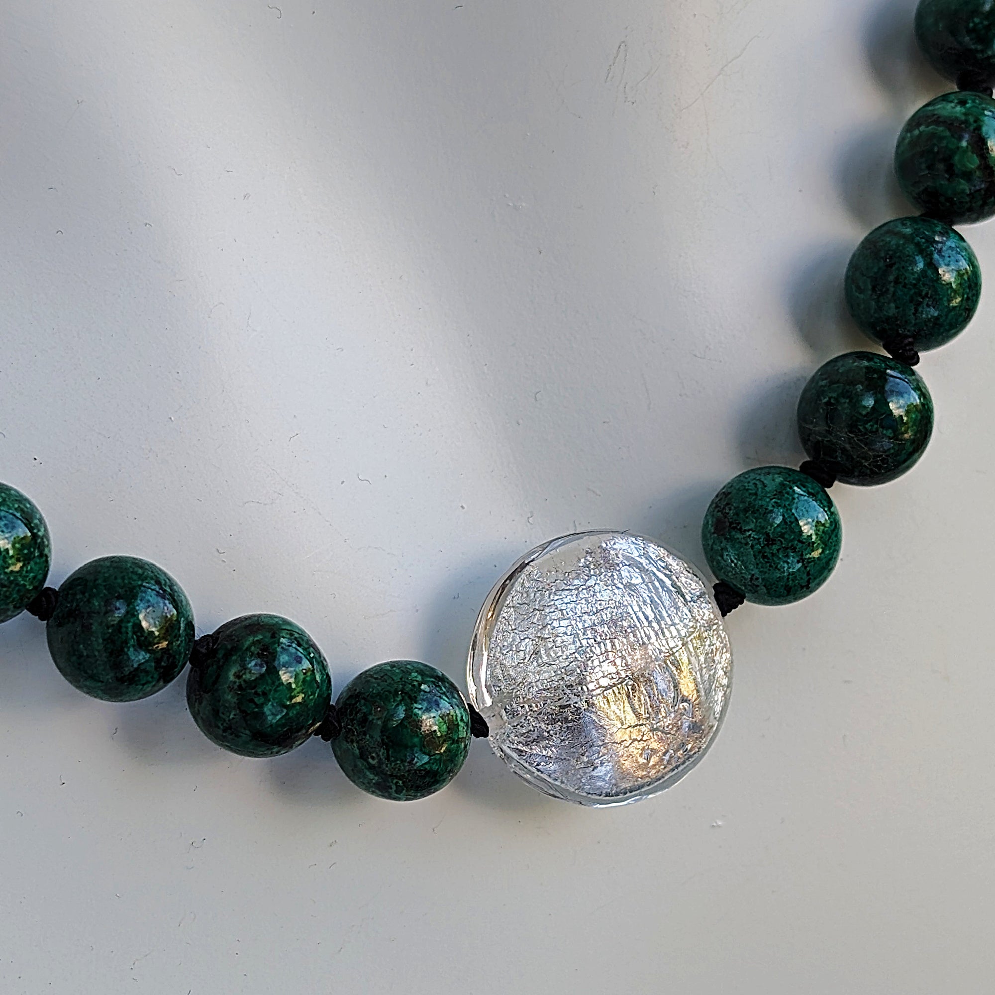 A close-up image of a silver toggle clasp on a necklace with hand-knotted chrysocolla beads and lampwork glass.