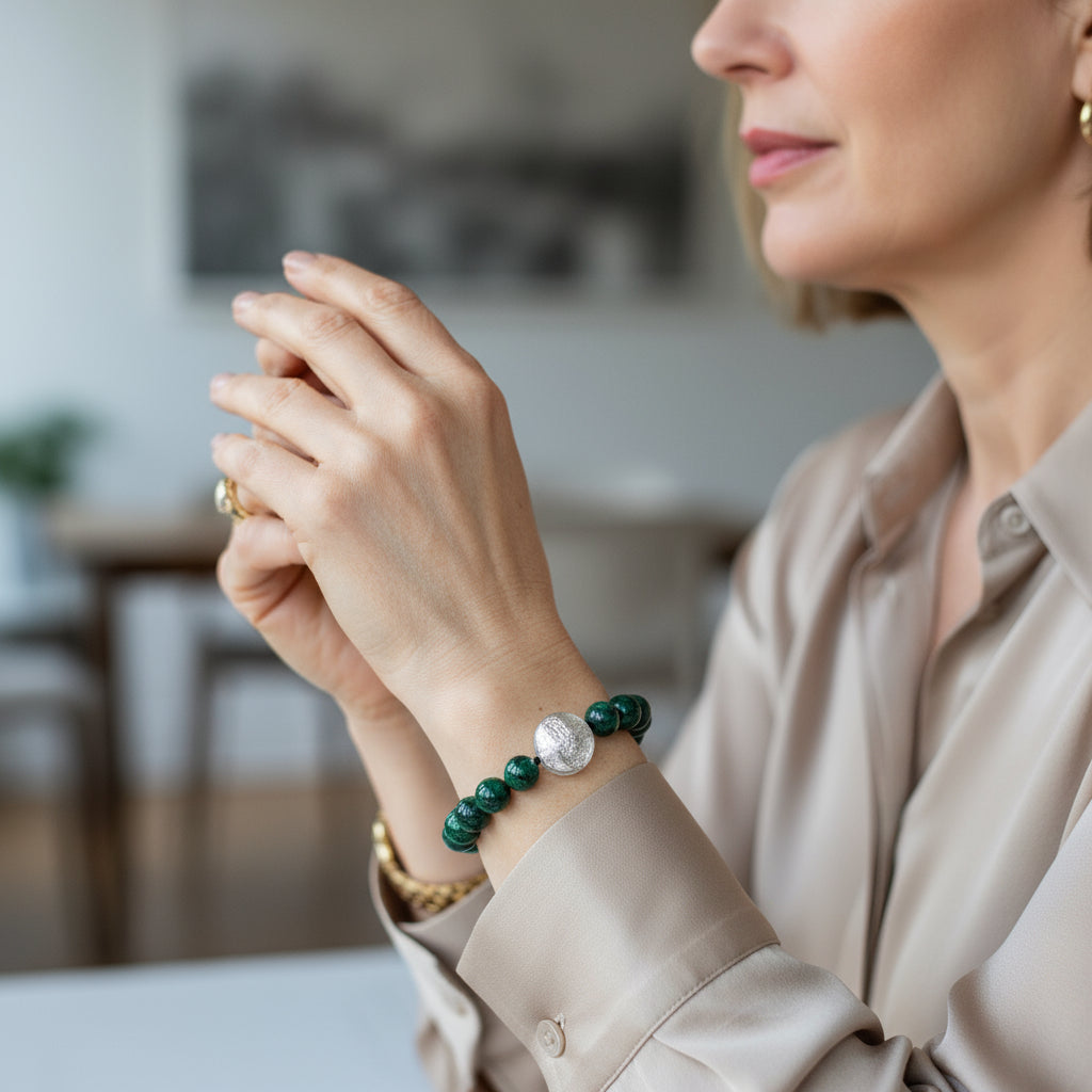Woman wearing a bracelet with green beads and a silver charm, sitting indoors.