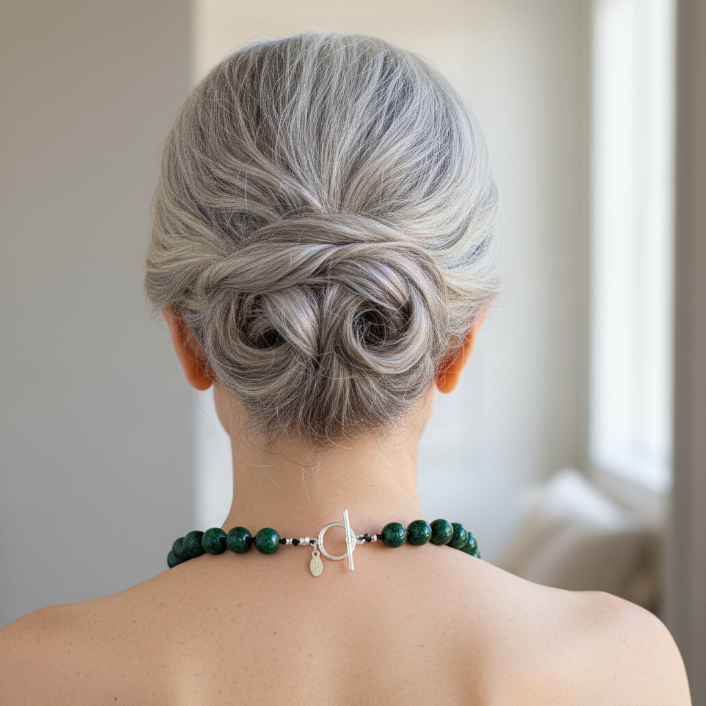 Person with styled gray hair wearing a green beaded necklace against a neutral background