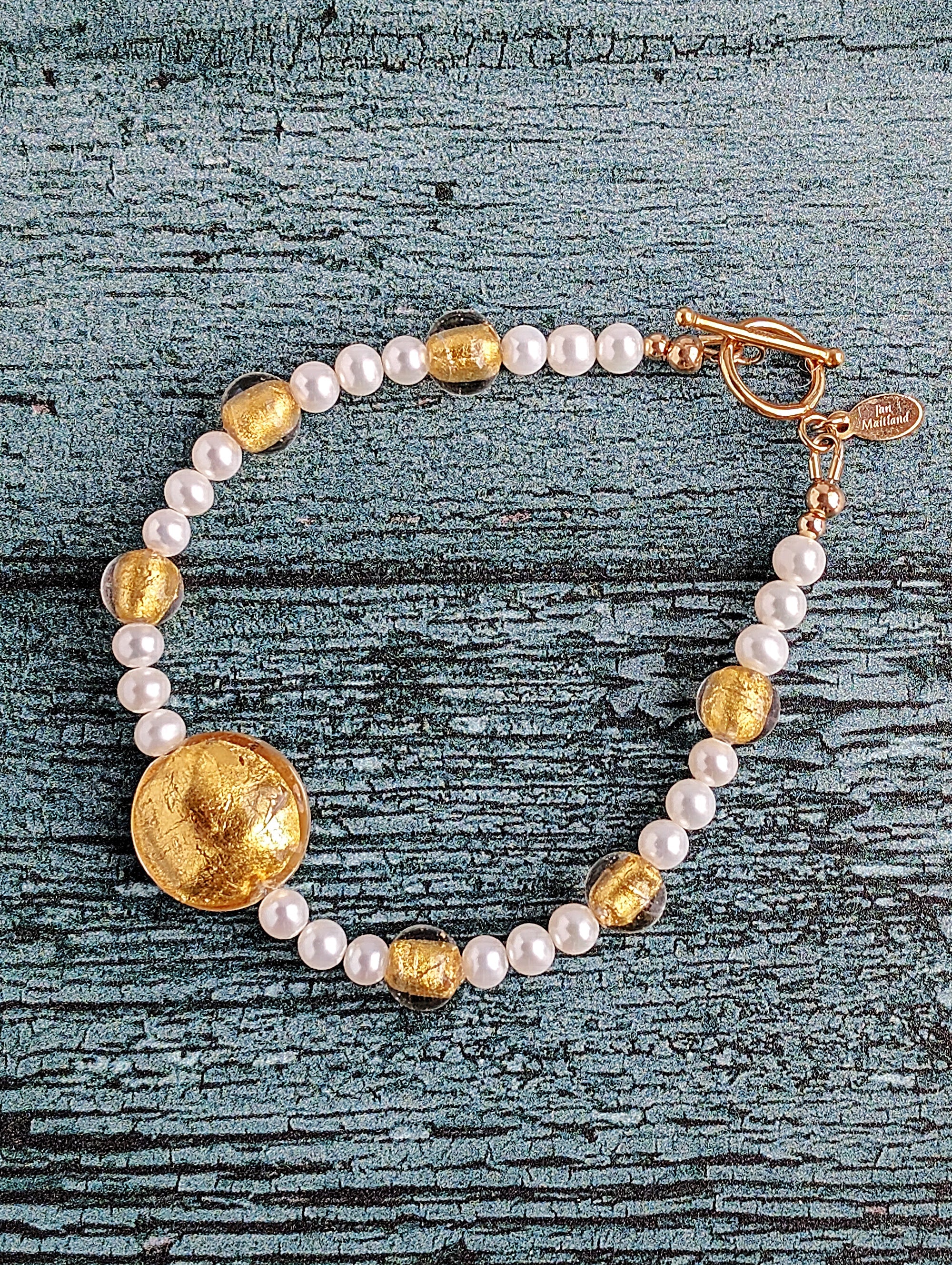 White pearl bracelet with gold Venetian lamp work glass beads, large center bead in 24 karat gold foil lamp work Venetian glass. The bracelet is finished with gold toggle clasp and designer tag.