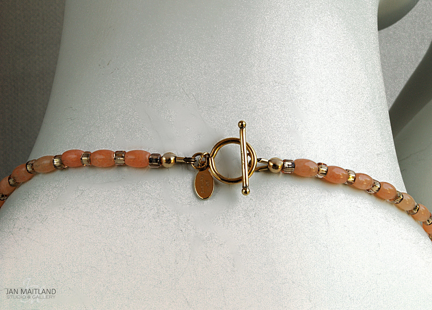 Close up of the gold and coral necklace toggle clasp on the back of the white mannequin neck.