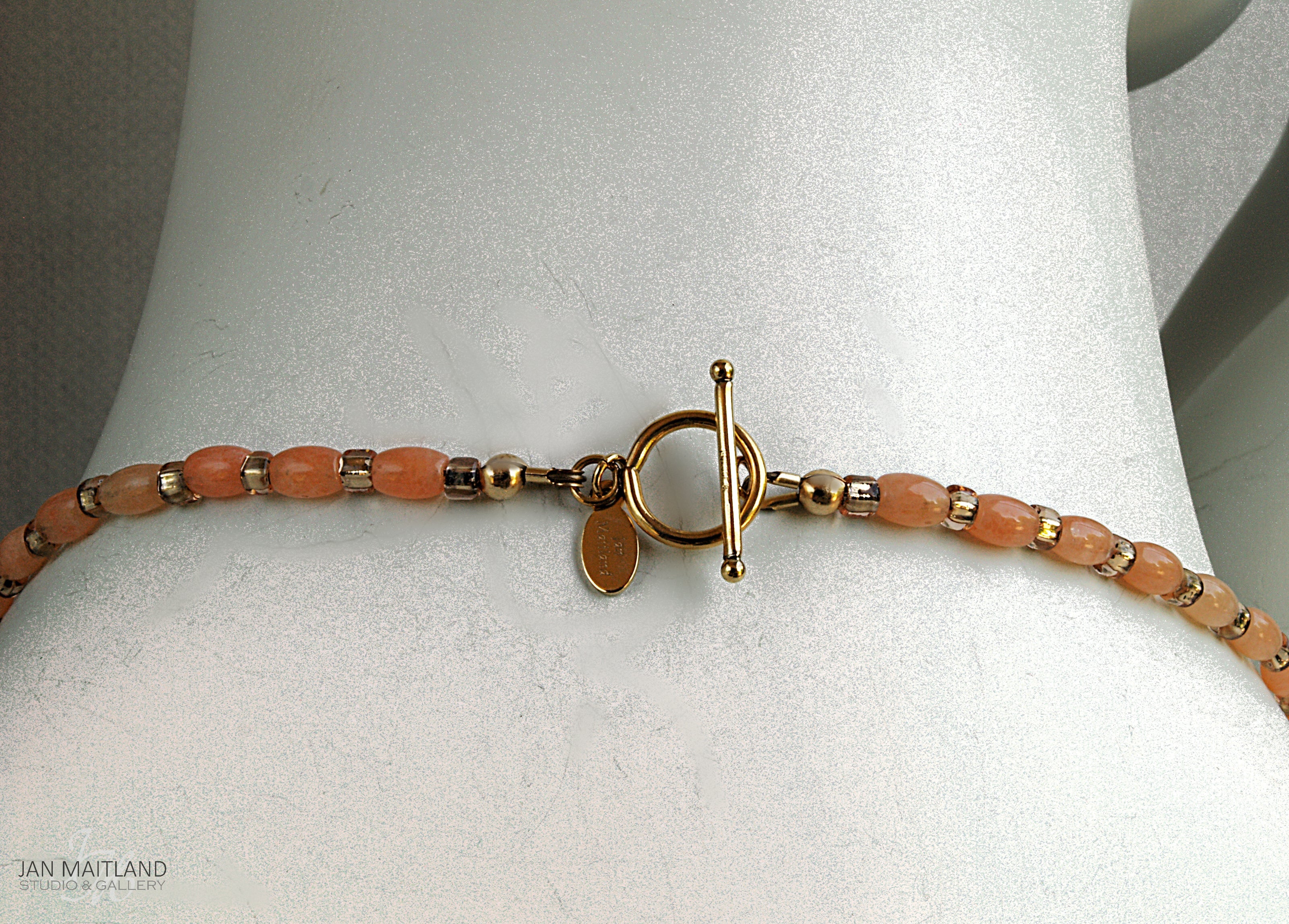 Close up of the gold and coral necklace toggle clasp on the back of the white mannequin neck.
