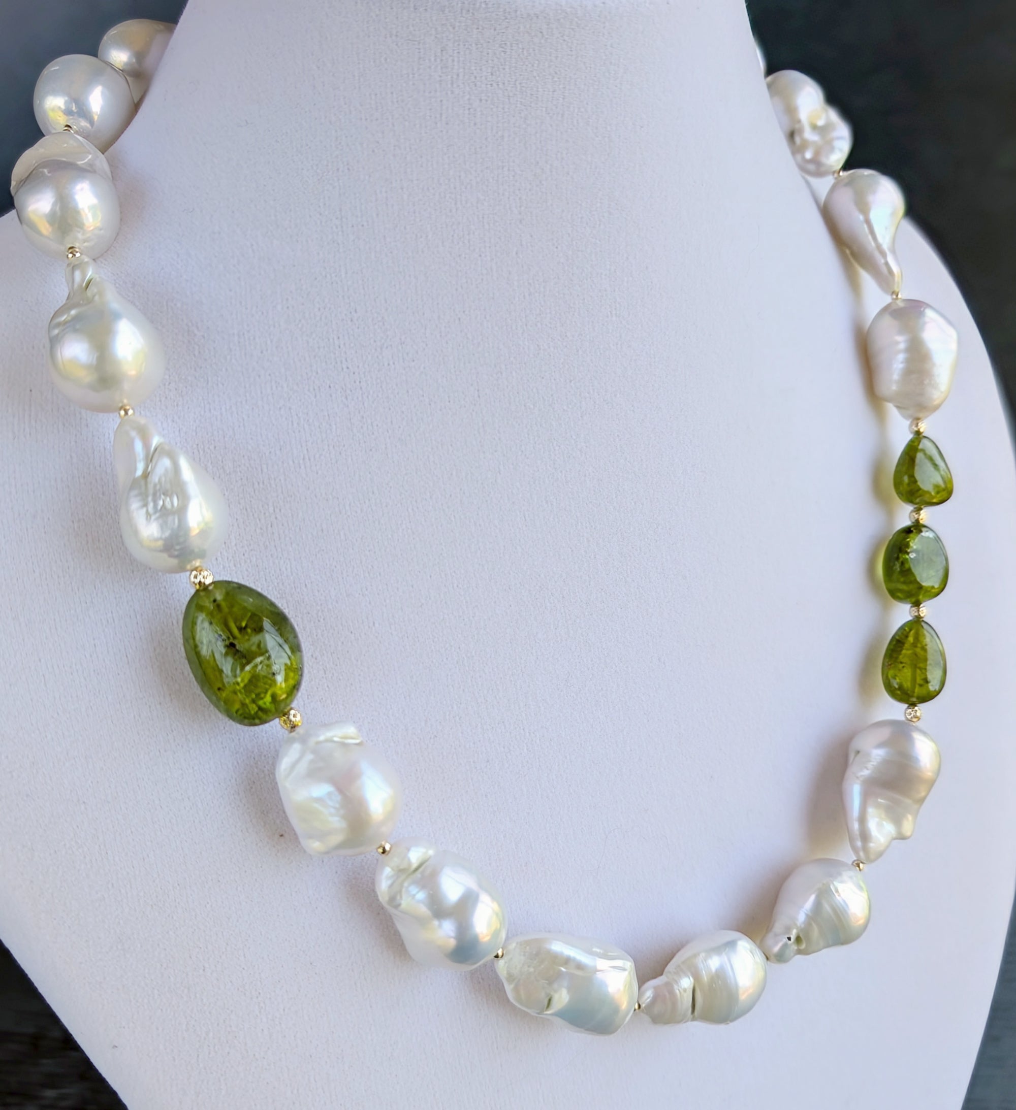 Baroque pearl, peridot and gold necklace measuring 19". The peridots are offset with three on one side of the necklace and one larger peridot on the opposite side. Between each pearl and peridot gem are 14 Karat gold beads. The necklace is pictured on a display neck.