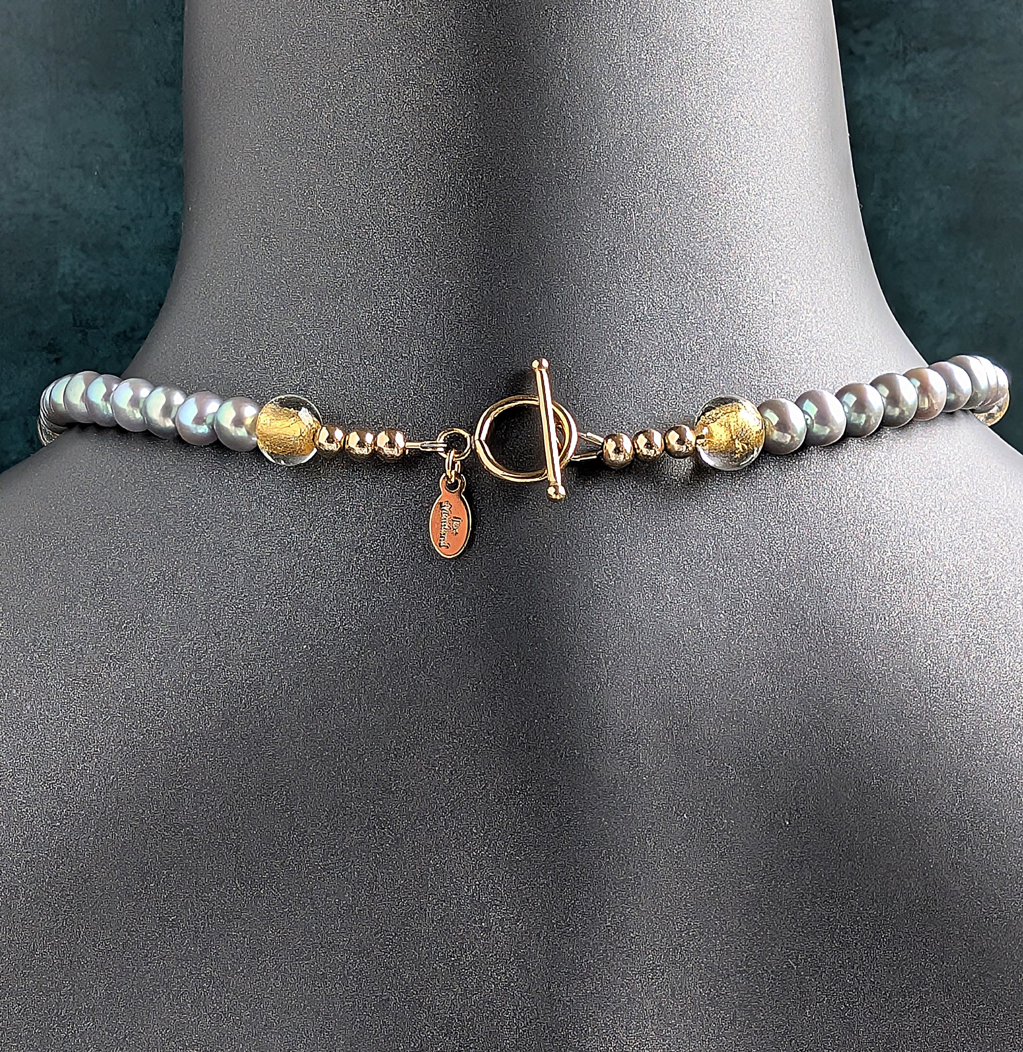 The back of Pearl and gold necklace showing the gold toggle clasp on a mannequin with a dark background
