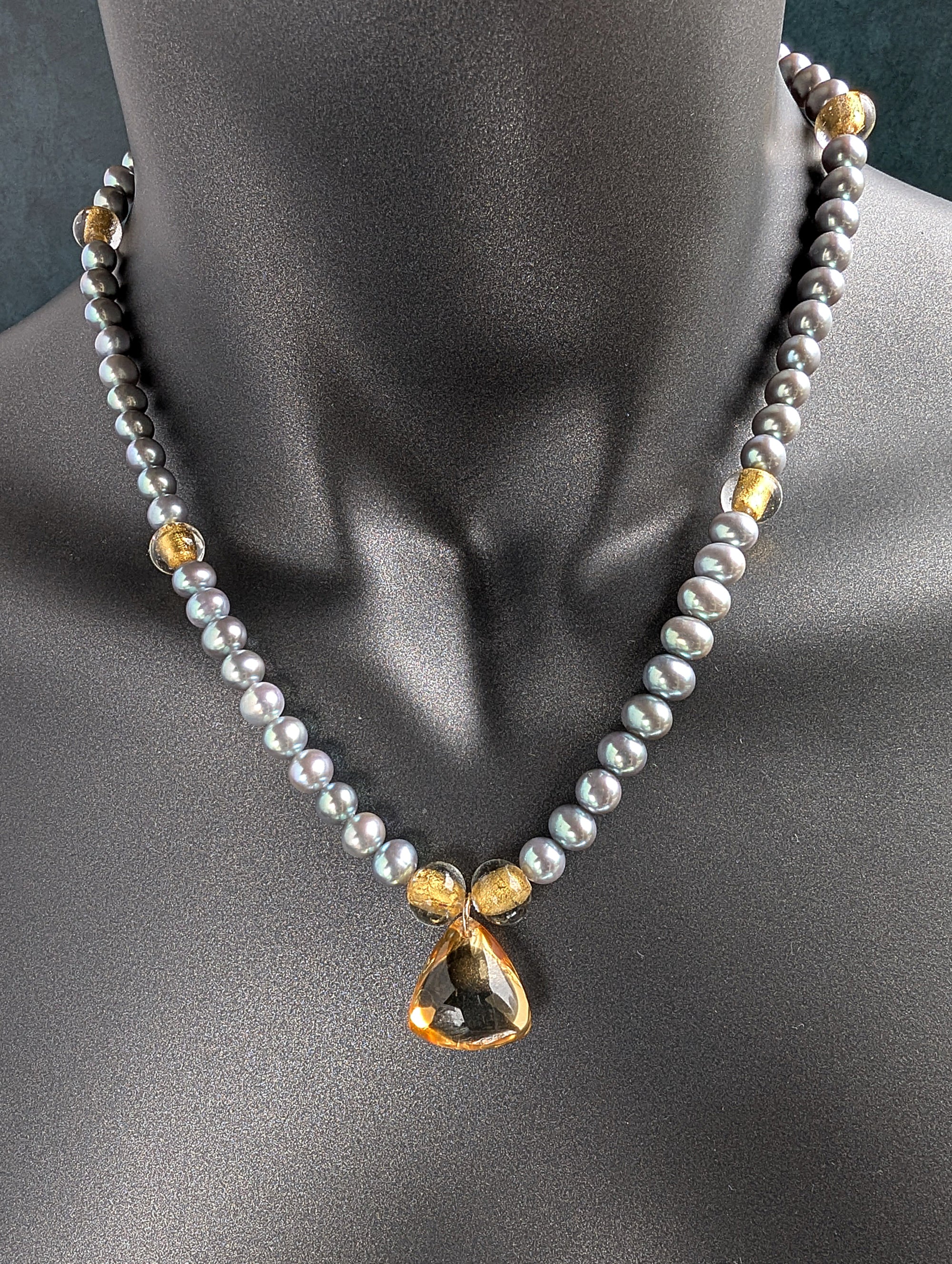 Necklace with gray pearls, citrine pendant and gold accents on a mannequin