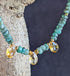 A necklace with green emerald beads and faceted citrine briolette gems, displayed against a tree trunk.
