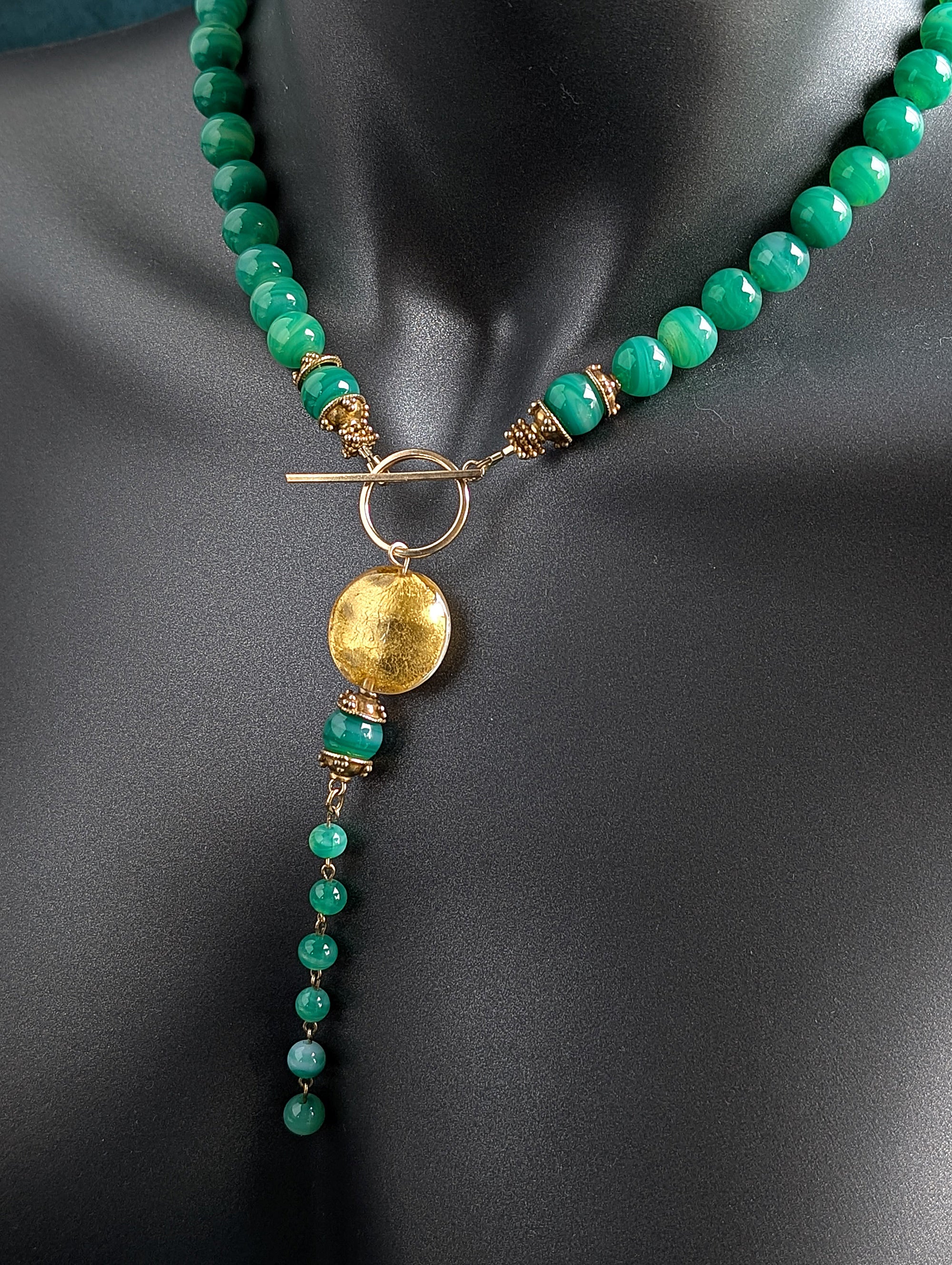 Necklace with green beads and gold accents on a mannequin.