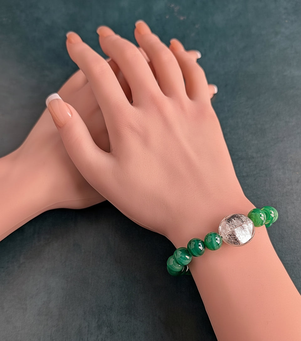 Hand wearing a green beaded bracelet with a round silver Venetian glass center piece.on a dark background