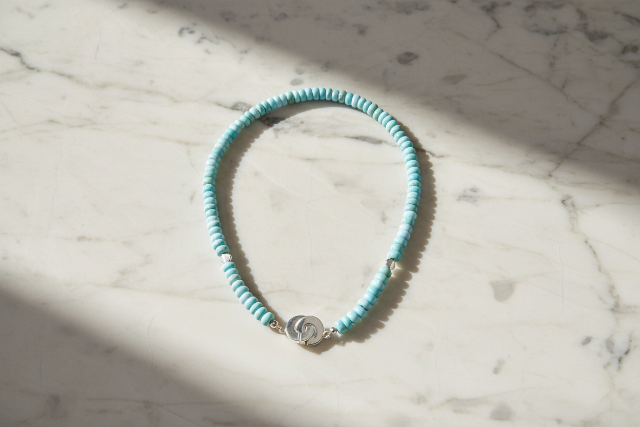 Necklace with light blue beads and a silver clasp on a white marble background