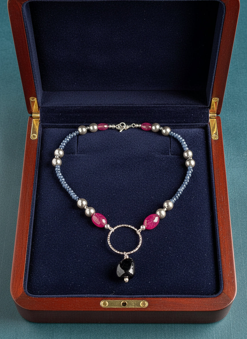 Necklace with blue, rose, and navy beads on a navy background in a wooden jewelry case.