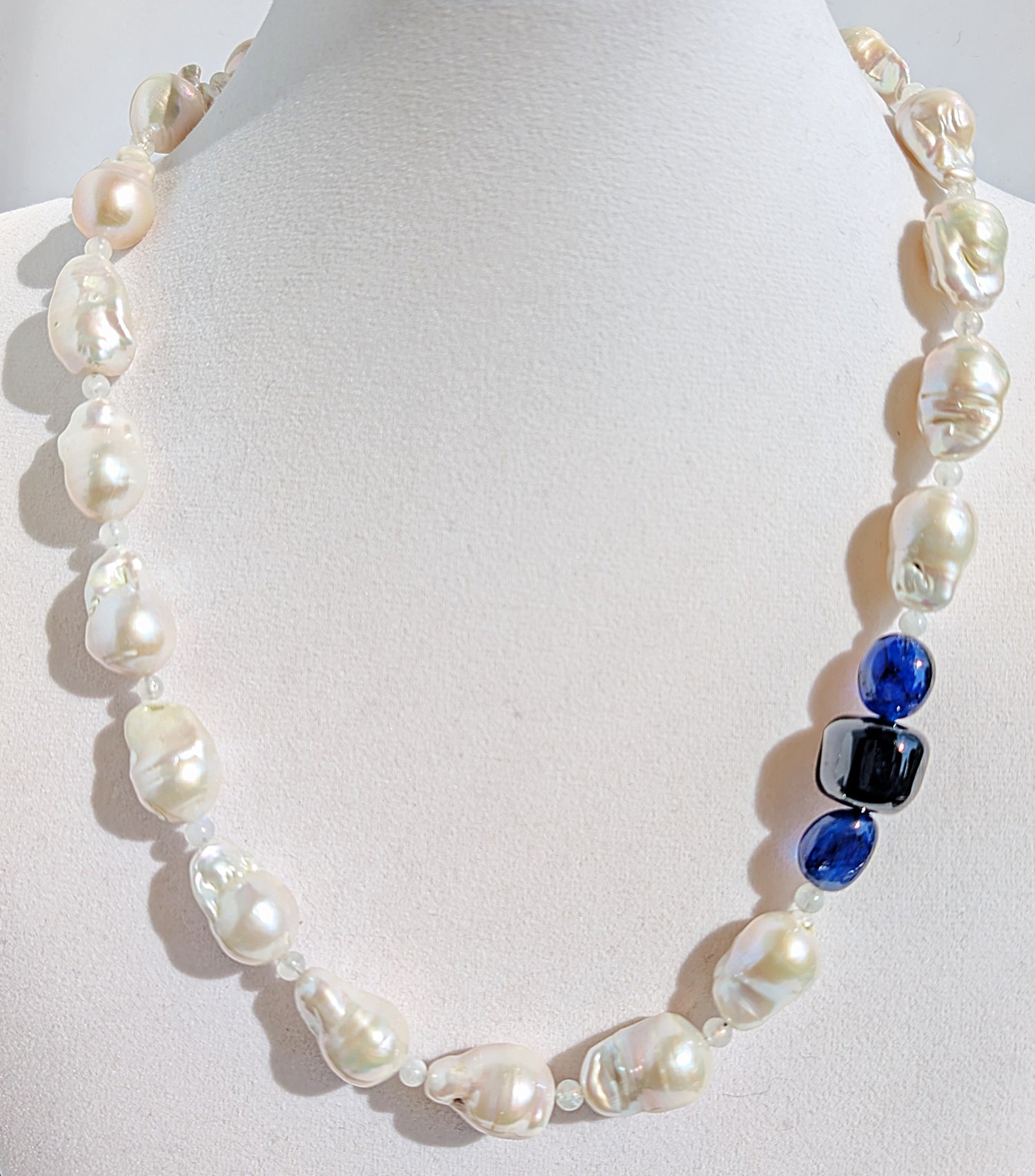 A close up of the baroque pearl, moonstone and sapphires on the necklace pictured on a display jewelry neck.
