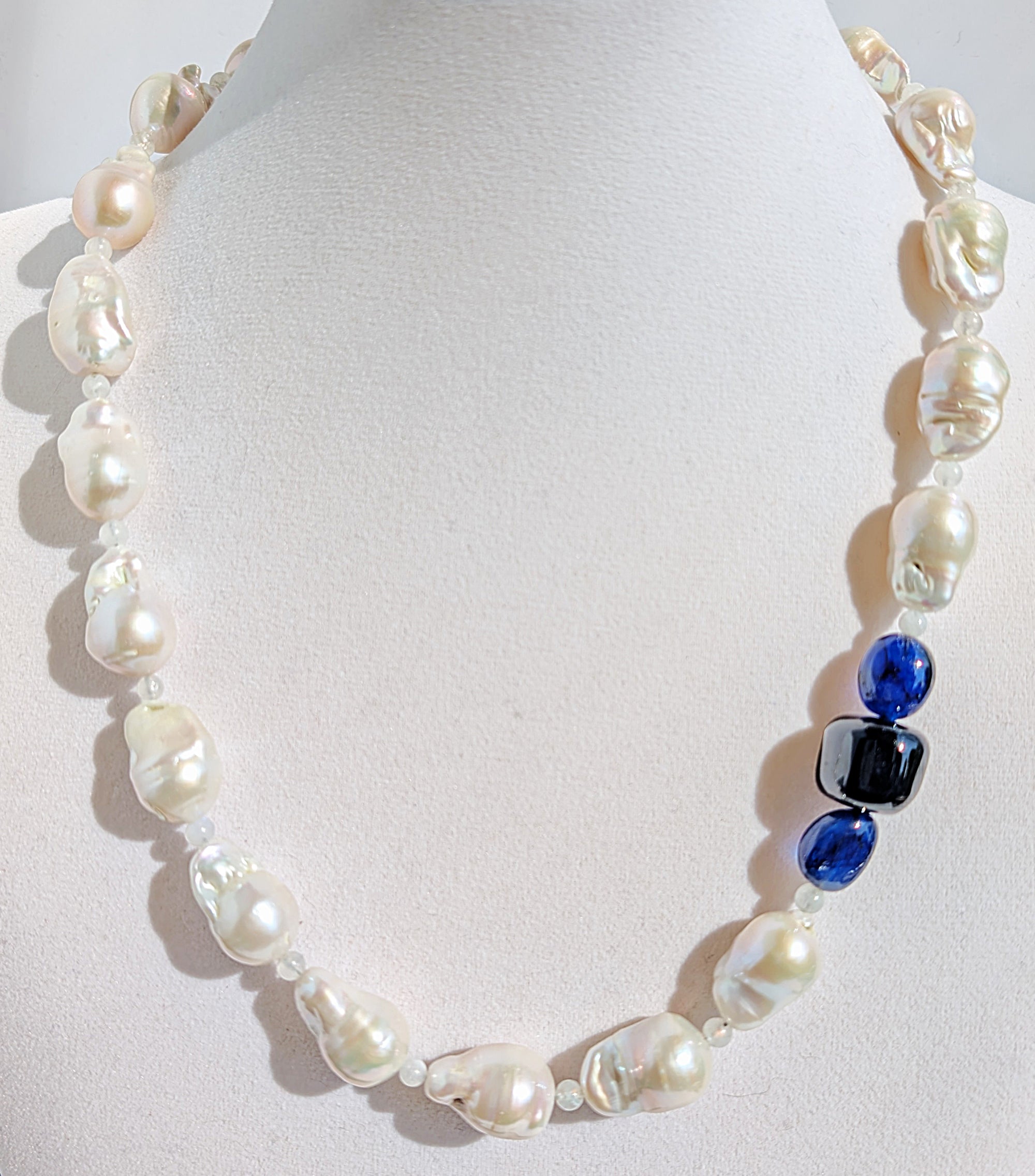 A close up of the baroque pearl, moonstone and sapphires on the necklace pictured on a display jewelry neck.