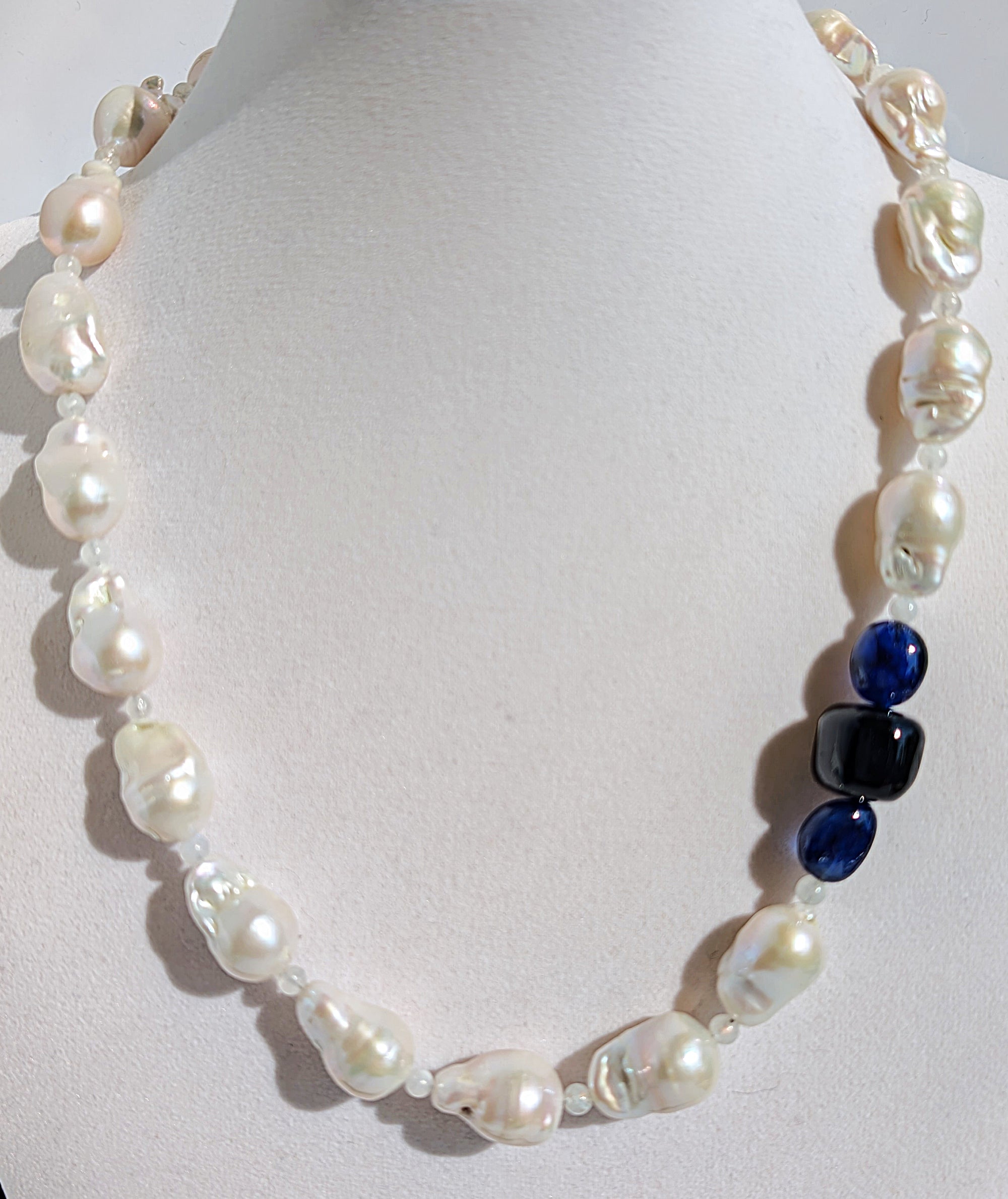 A close up of the baroque pearl, moonstone and sapphires on the necklace pictured on a display jewelry neck.