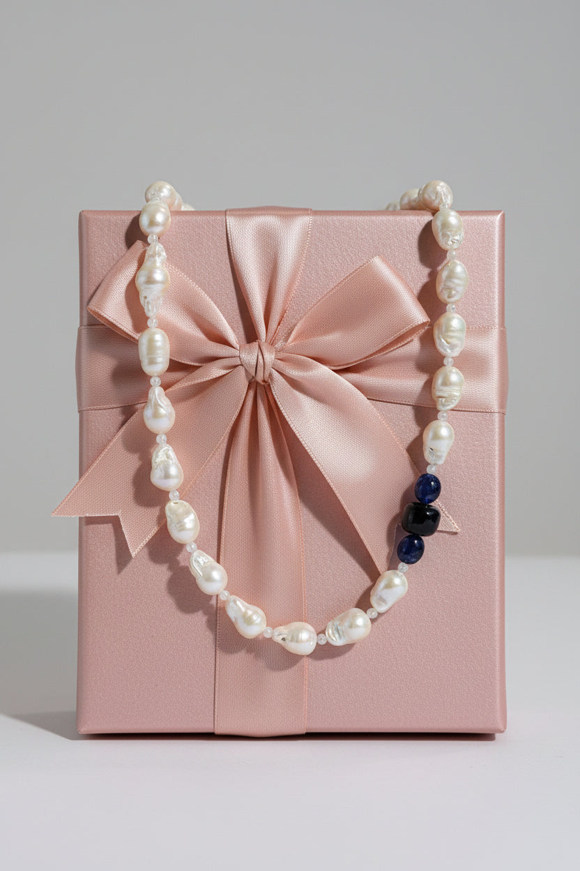 A close up of the baroque pearl, moonstone and sapphires on the necklace pictured on a display jewelry gift box.