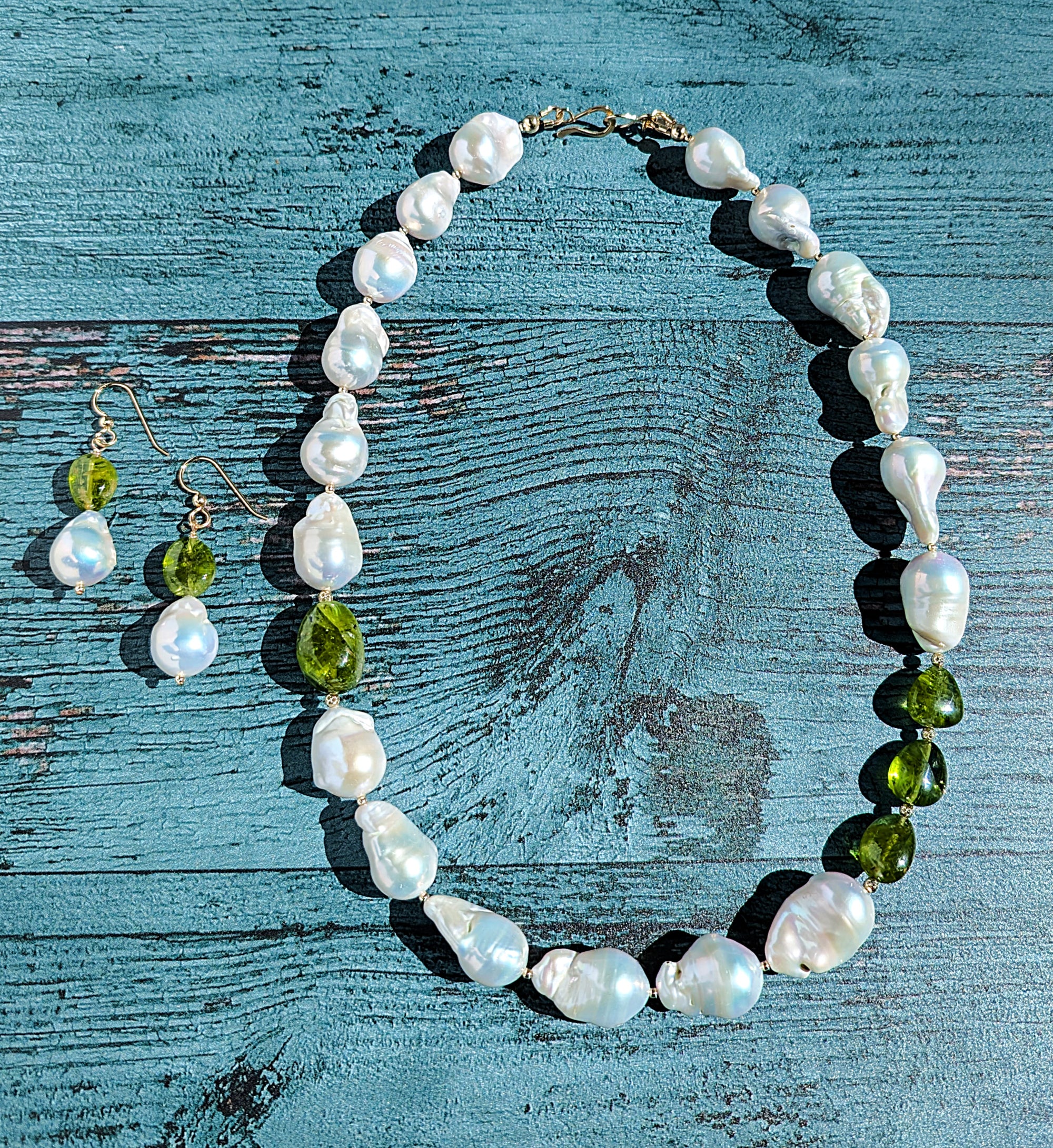 Baroque pearl, peridot and gold necklace measuring 19". The peridots are offset with three on one side of the necklace and one larger peridot on the opposite side. Between each pearl and peridot gem are 14 Karat gold beads and the necklace is finished with a 14 Karat hook and eye clasp. Matching dangle earrings are also pictured with the necklace.