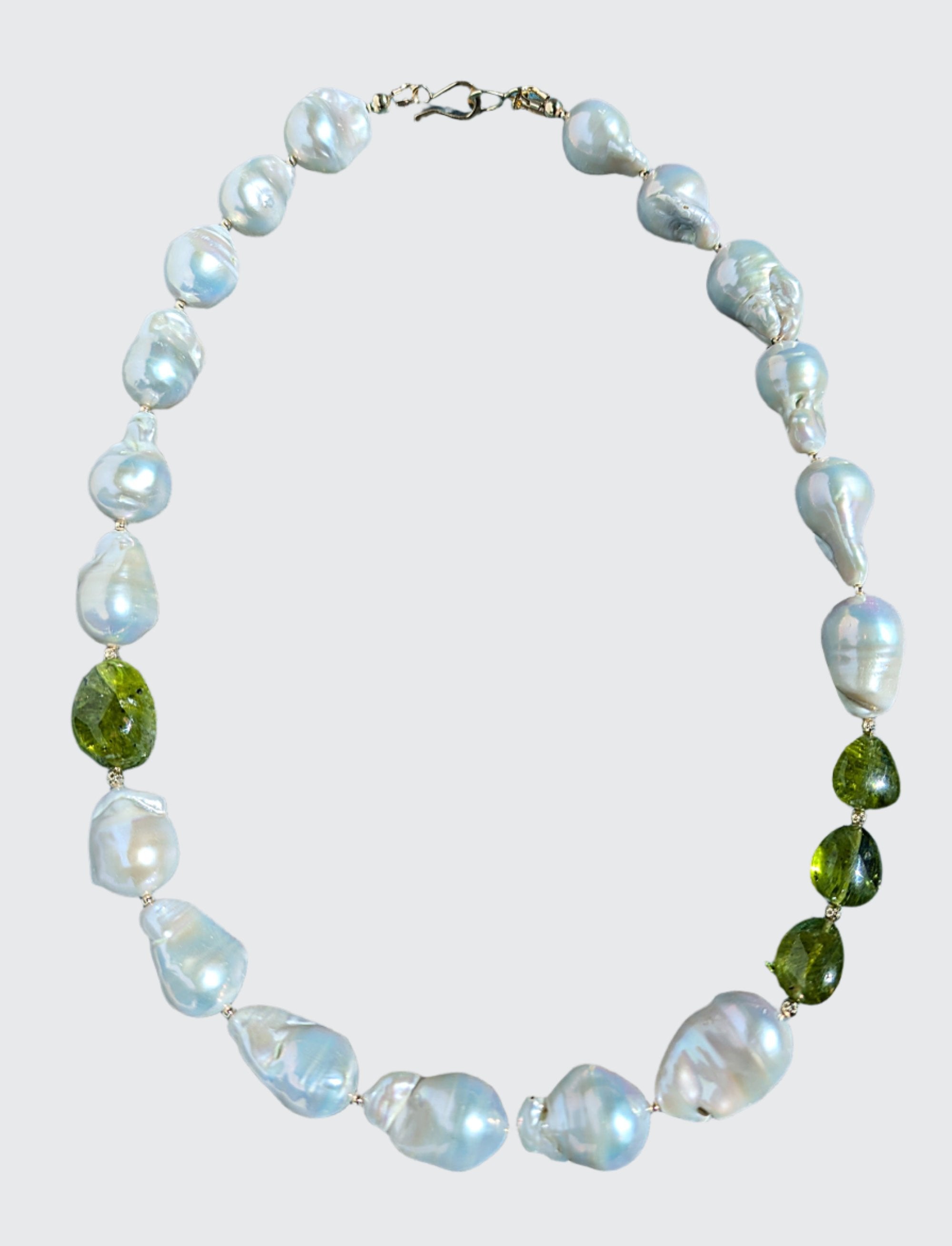 Baroque pearl, peridot and gold necklace measuring 19". The peridots are offset with three on one side of the necklace and one larger peridot on the opposite side. Between each pearl and peridot gem are 14 Karat gold beads and the necklace is finished with a 14 Karat hook and eye clasp.