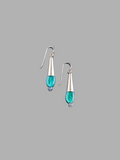 This image displays a pair of elegant Emerald Drop Earrings. The earrings feature a sleek, hanging design with each consisting of a polished metal droplet, from which a vibrant green emerald gemstone dangles like a delicate pendant.