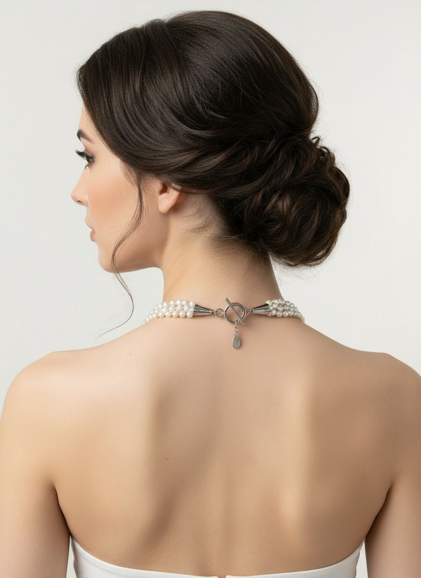 Woman wearing a pearl necklace with a silver clasp on a plain background