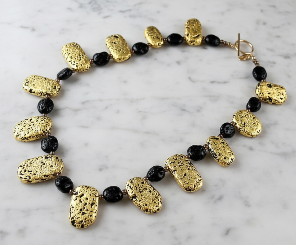 A luxurious necklace featuring hand-gilded luminous gold on lava stone, with a variety of shapes and sizes of gold-leaf-covered stones, and a gold-filled toggle clasp.