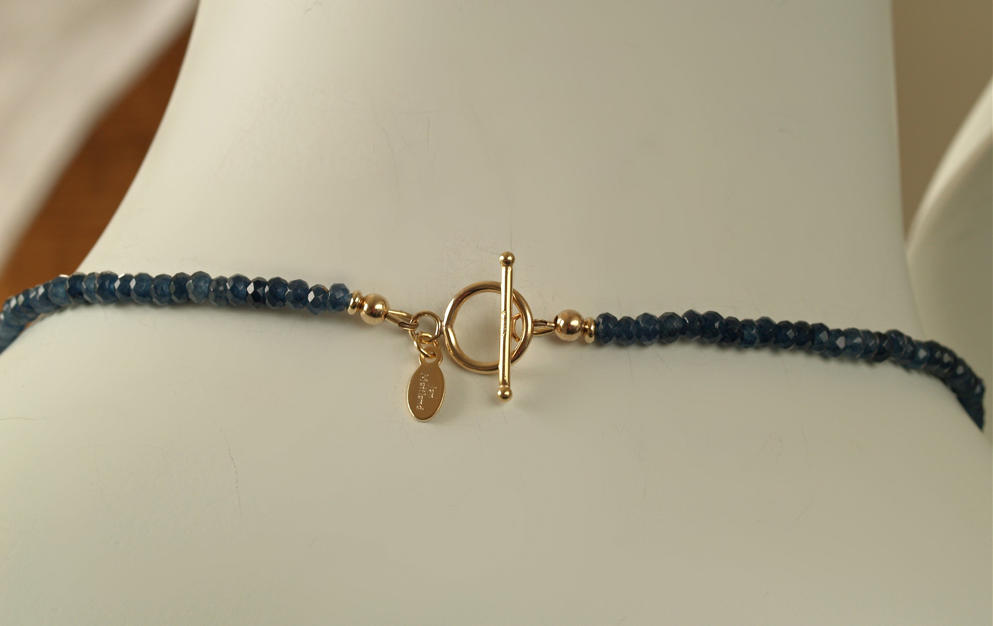 back of necklace showing the 14 karat gf toggle clasp and designer signature tag, and 4mm sparkly faceted dark blue onyx close up on mannequin neck