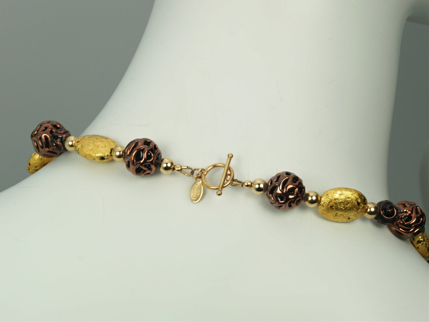 Hand made necklace with 23 karat gold gilded lava stones, lamp work bronze Czech glass, and 14 karat gold filled small round beads. The necklace is finished with 14 karat gold filled toggle clasp. The necklace is photographed on a white mannequin&