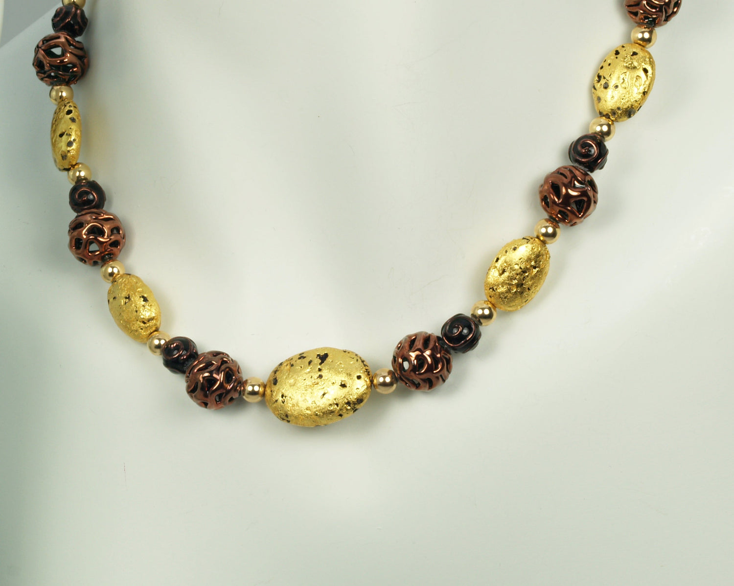 Hand made necklace with 23 karat gold gilded lava stones, lamp work bronze Czech glass, and 14 karat gold filled small round beads. The necklace is finished with 14 karat gold filled toggle clasp. The necklace is photographed on a white mannequin.