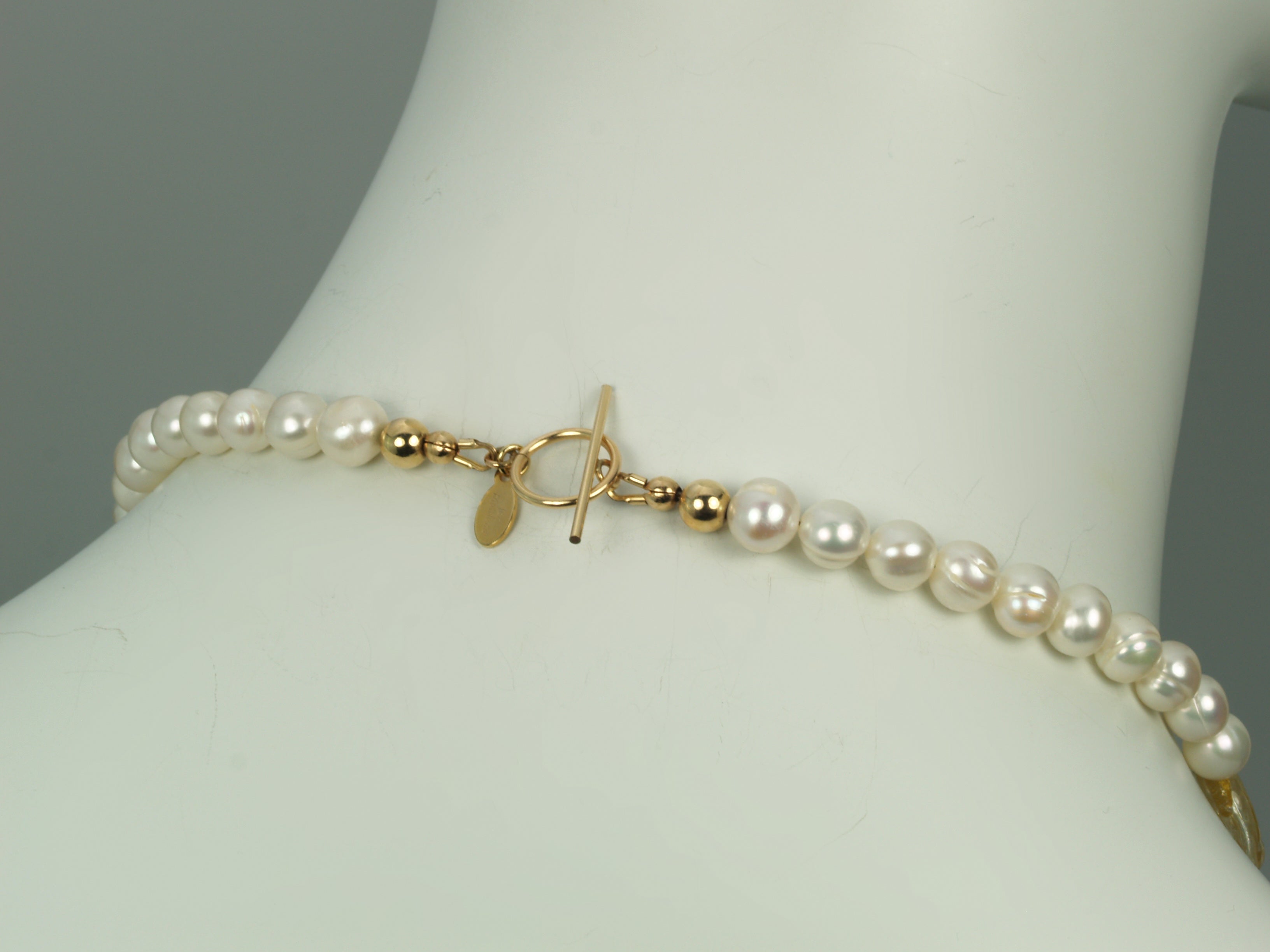 Back of pear necklace showing gold toggle clasp and designer tag featured on a mannequin neck.
