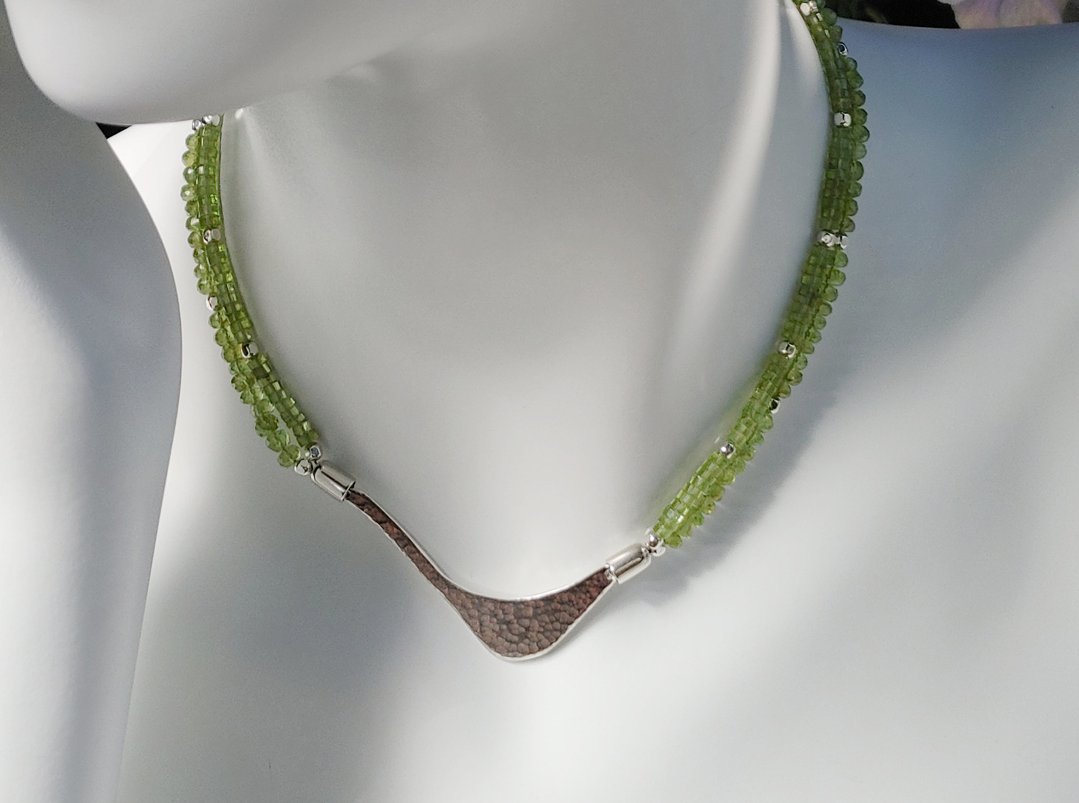 Hammered silver abstract pendant necklace with two strands of faceted peridot and silver beads. The necklace is finished with a magnetic clasp and the artist&