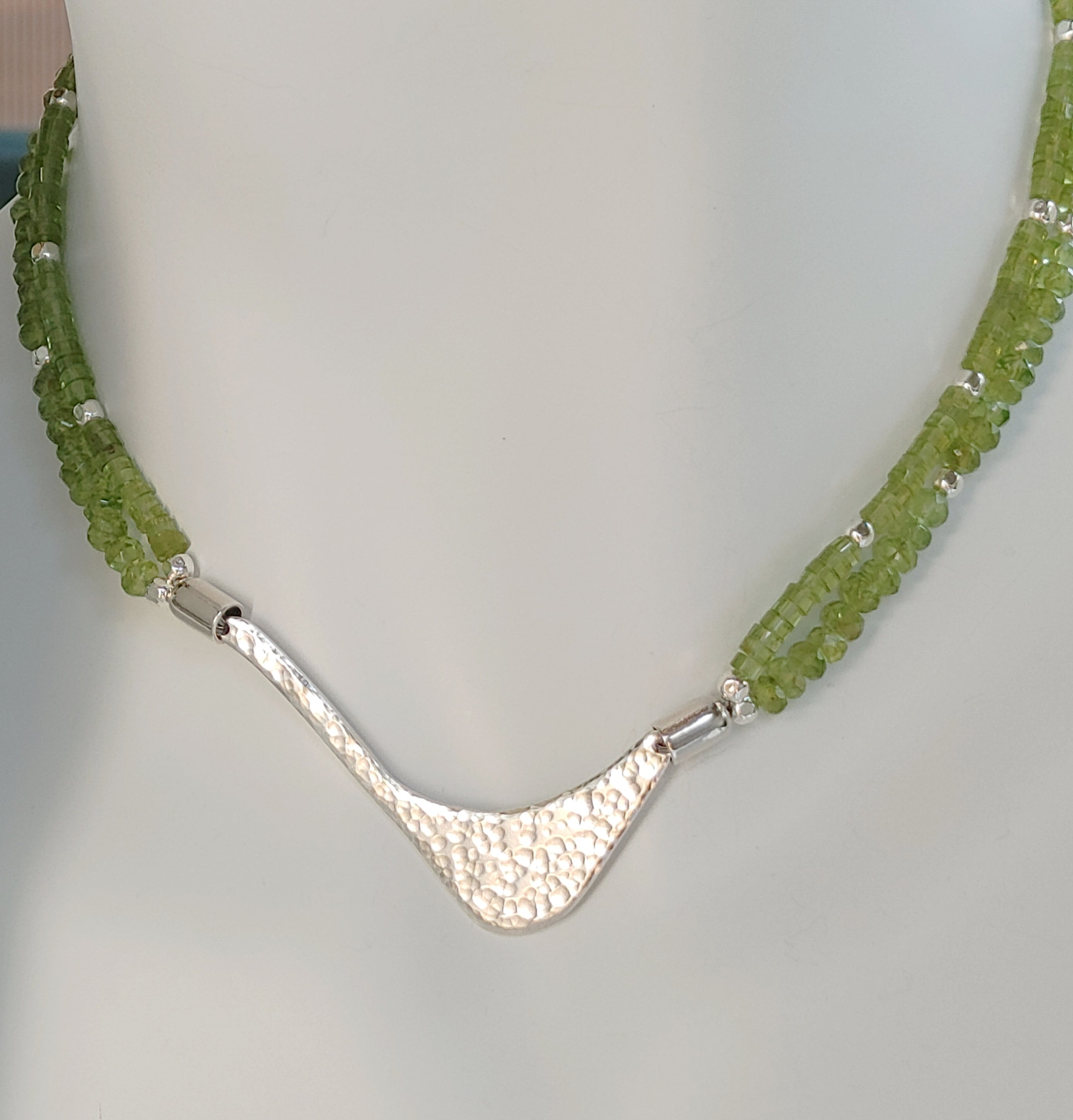 Hammered silver abstract pendant necklace with two strands of peridot and silver beads. The necklace is finished with a magnetic clasp and the artist&