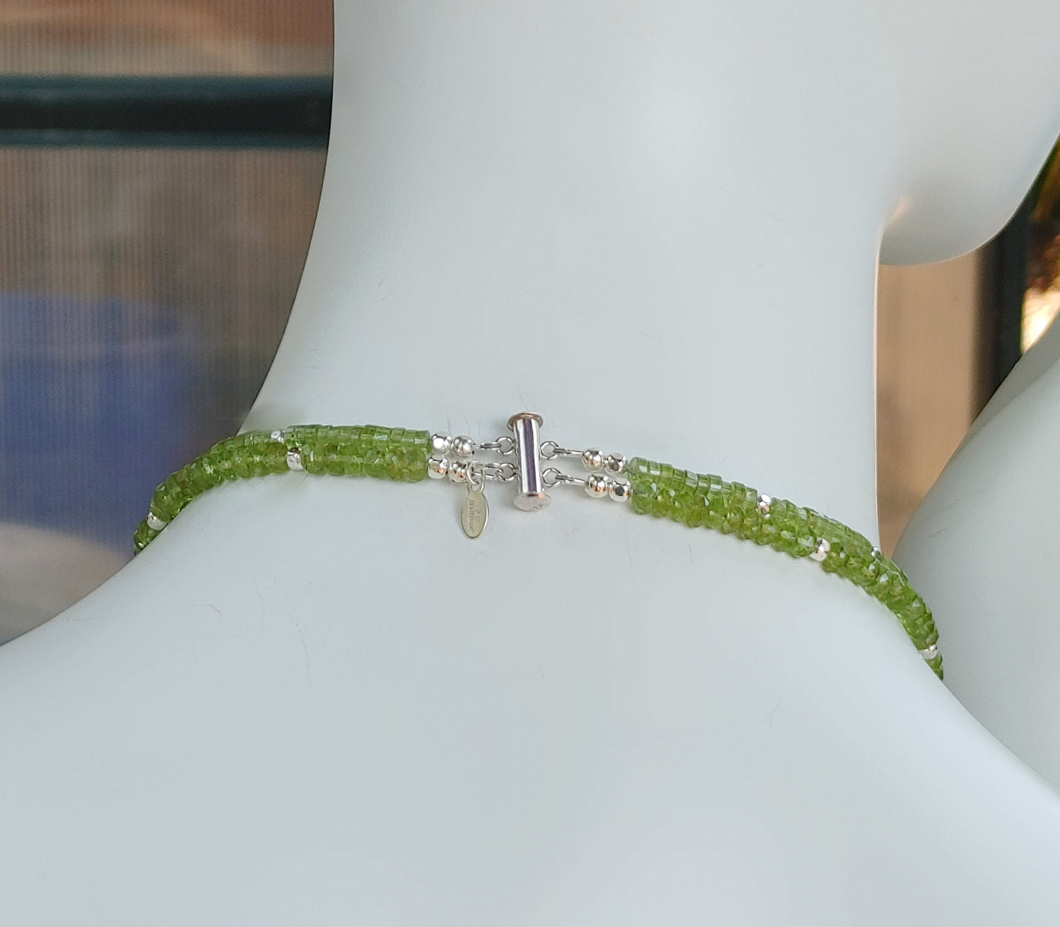 Hammered silver abstract pendant necklace with two strands of faceted peridot and silver beads. The necklace is finished with a magnetic clasp and the artist&