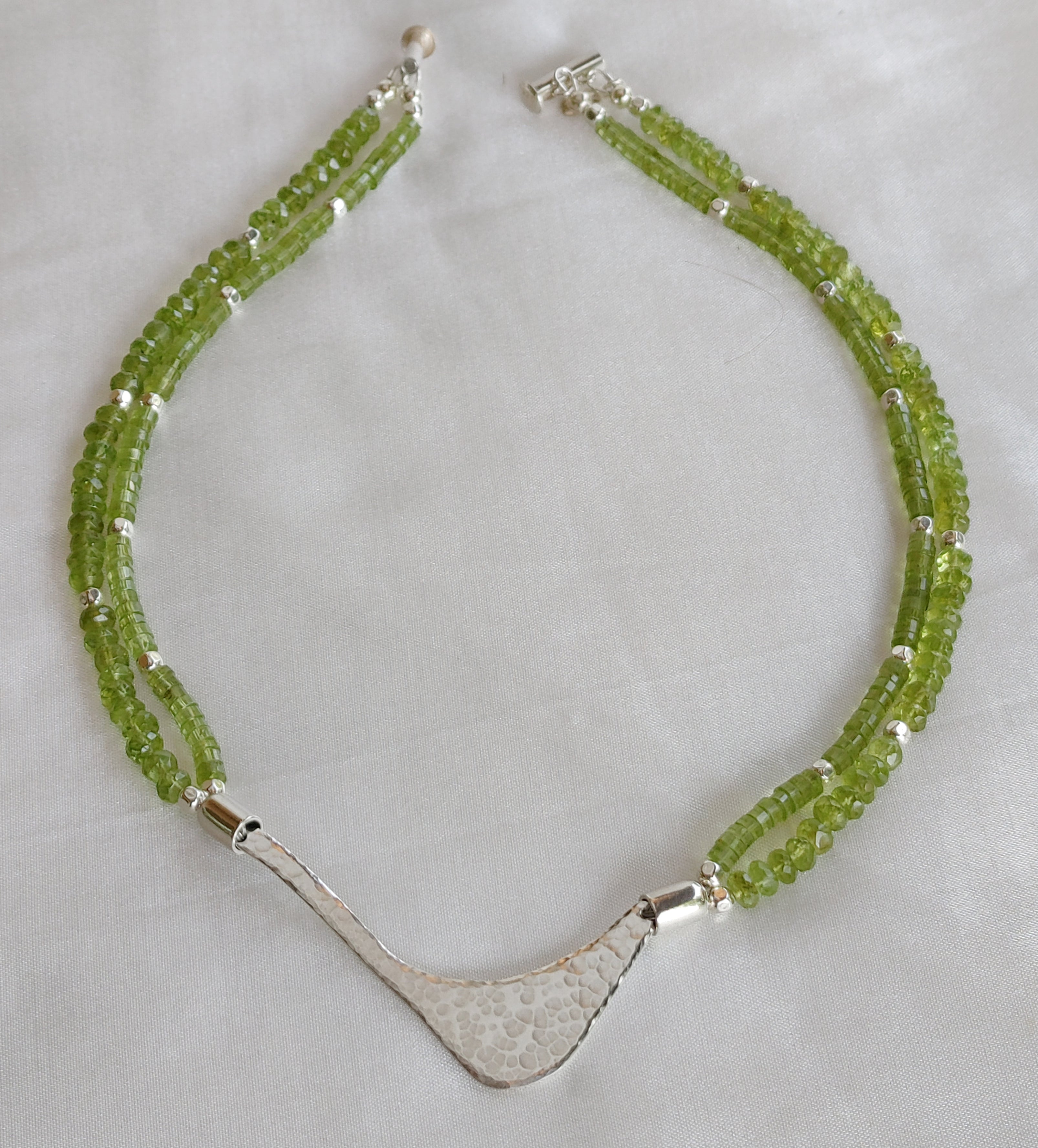 Hammered silver abstract pendant necklace with two strands of peridot and silver beads. The necklace is finished with a magnetic clasp and the artist&