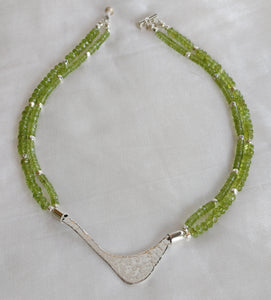Hammered silver abstract pendant necklace with two strands of peridot and silver beads. The necklace is finished with a magnetic clasp and the artist's signature tag. The necklace measures 17" (43.18cm). The necklace is displayed, in full, on a white background