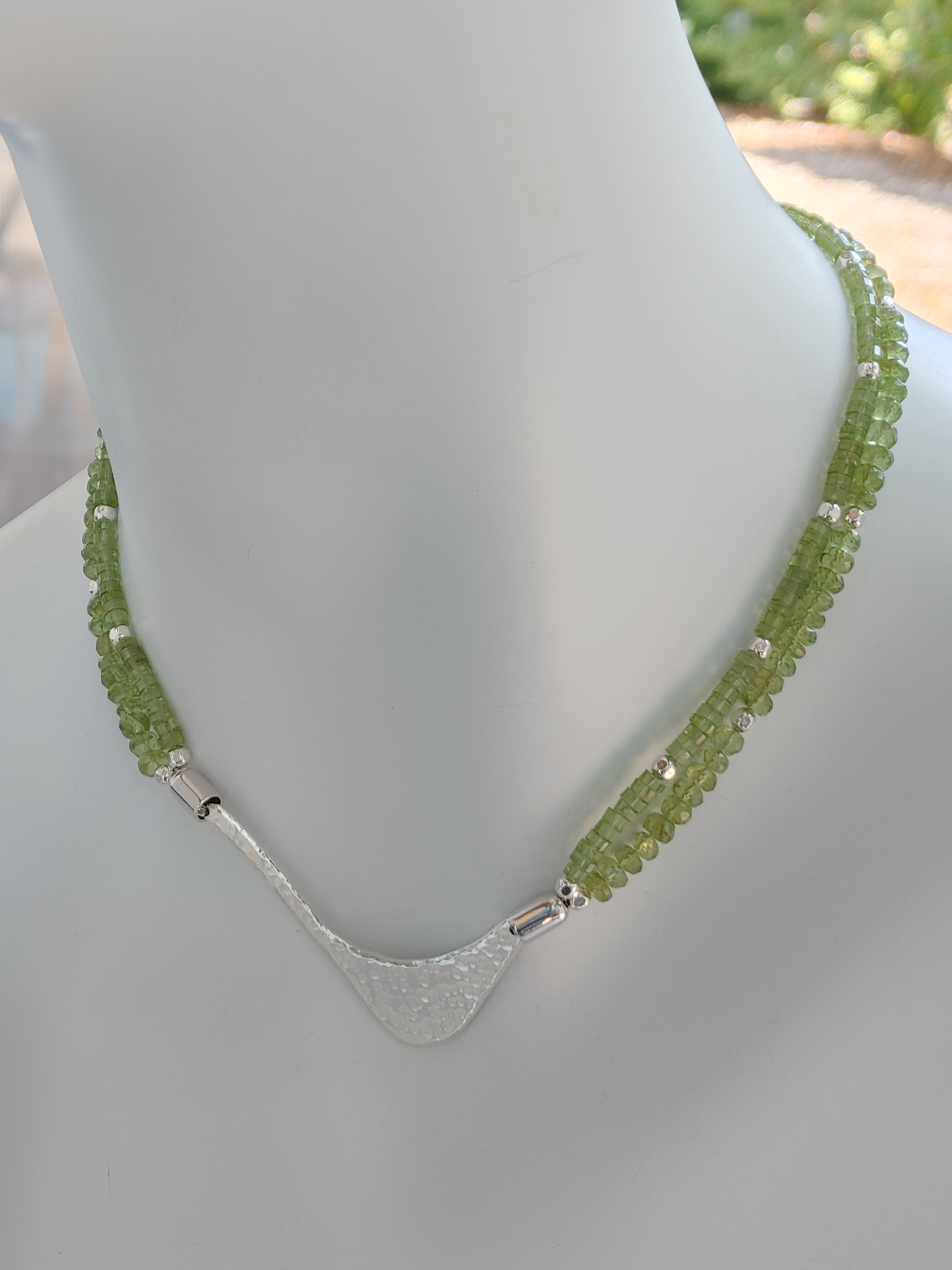 Hammered silver abstract pendant necklace with two strands of peridot and silver beads. The necklace is finished with a magnetic clasp and the artist&