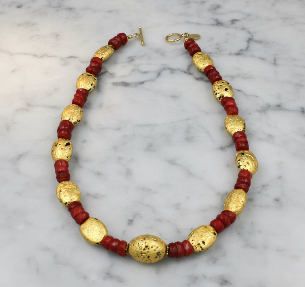 Necklace with red and gold beads on a white marble table.