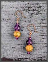 Load image into Gallery viewer, Amethyst Glow Earrings featuring faceted and smooth round  amethyst beads along with 23 karat hand gilded round lava stone. The earrings are 1.50&quot; and the drop is 1&quot;. They are on 14 karat gold filled french wire for pierced ears.