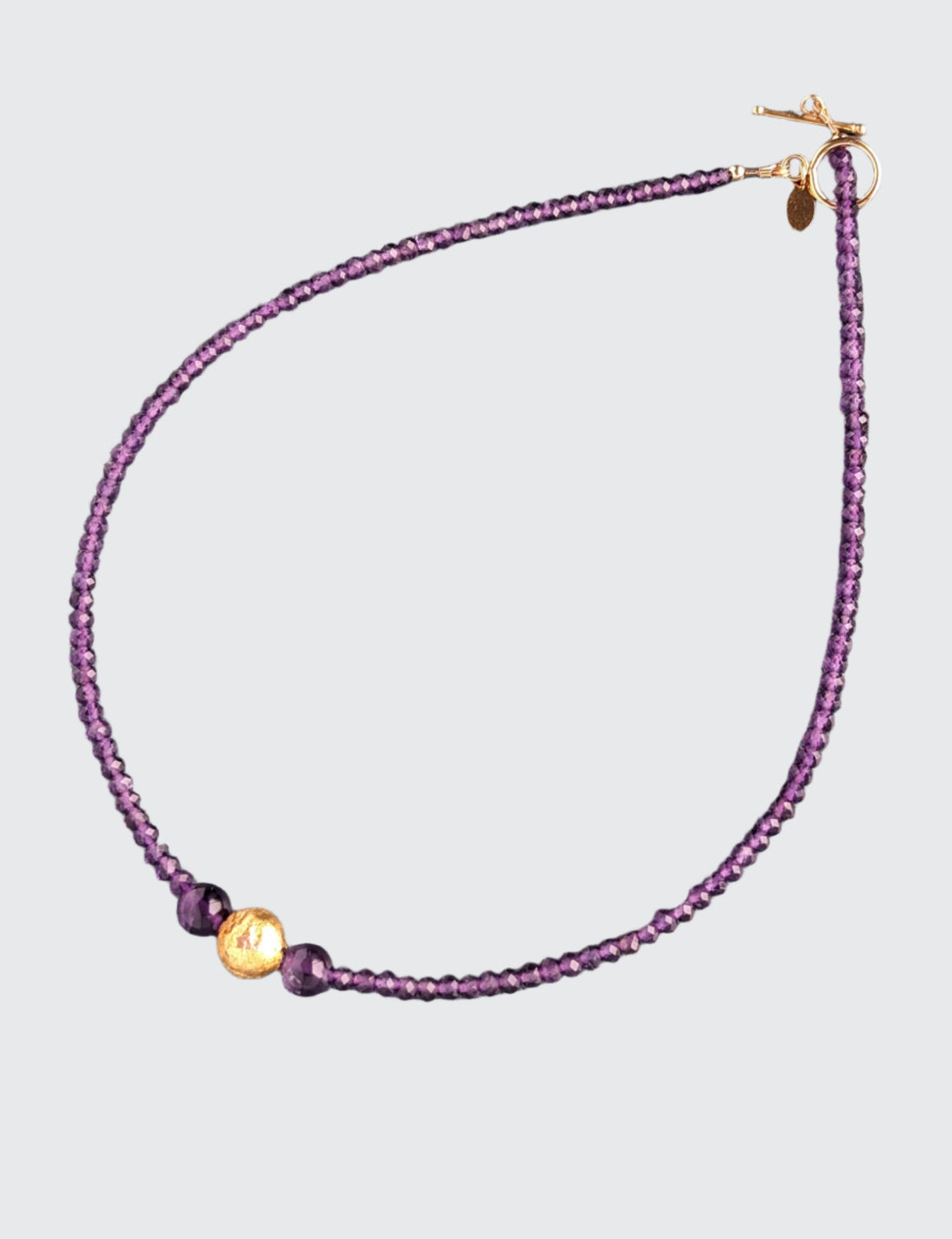 Amethyst Glow Necklace. Handcrafted with exquisite attention to detail, this elegant piece features stunning amethyst gemstones complemented by hand-gilded 23 karat gold leaf on lava stone center bead. It measures 17-inch in length and is finished with a 14 karat gold-filled toggle clasp.