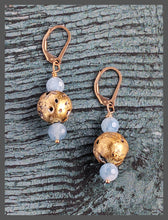 Load image into Gallery viewer, The Aquamarine Glow earrings are lightweight drop earrings featuring light blue aquamarine beads and 23-karat gold leaf on lava stones. They have a dainty, heirloom-like quality with a natural and elegant texture. The faceted aquamarine beads and 14-karat gold-filled leverback findings add delicate charm. The earrings measure 1.5&quot; (3.81cm) in dangle drop, 