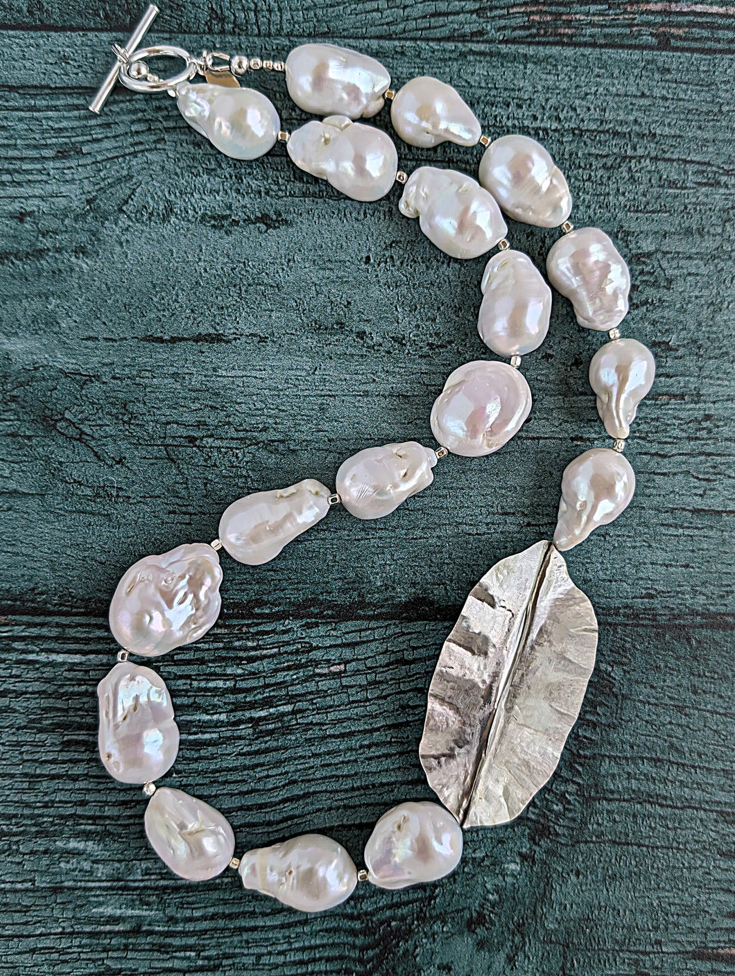 White Baroque pearl and silver necklace with hammered and fold form leaf design in silver with small silver beads in between each pearl. Necklace is finished with silver toggle clasp and designer tag.