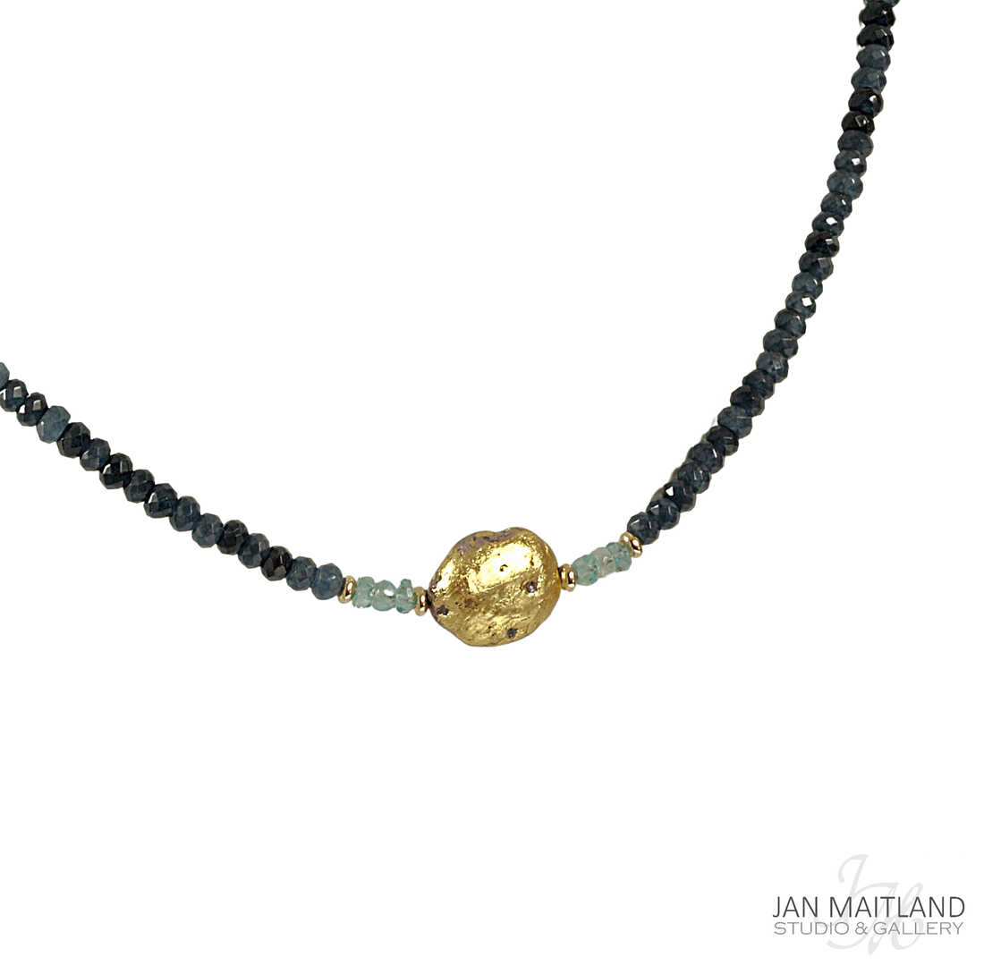 A gold-colored pendant necklace with blue faceted onyx and aqua apatite stones, displayed against a black background.