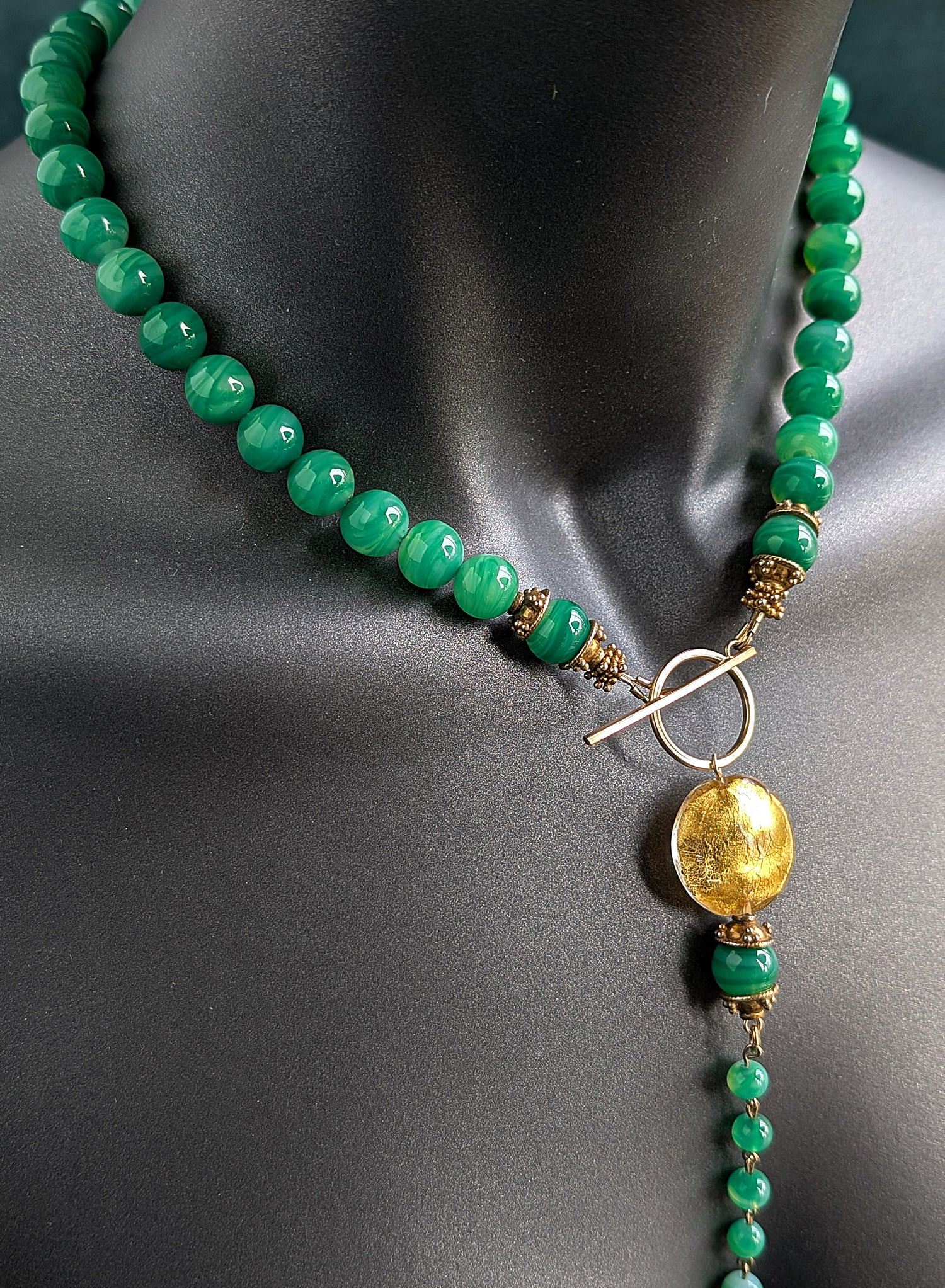Green beaded necklace with a gold pendant on a mannequin.