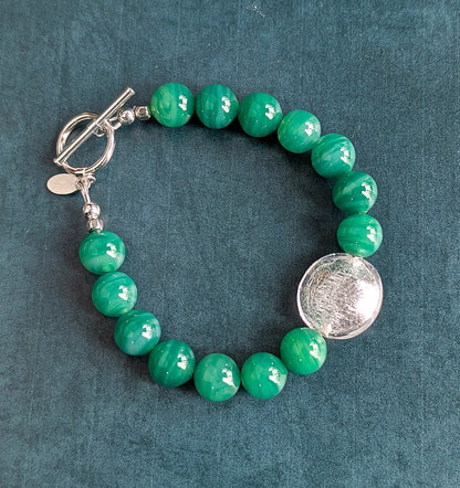 Green beaded bracelet with a silver clasp on a teal background
